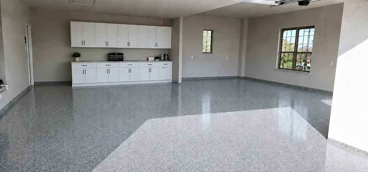 Spacious garage featuring a speckled epoxy floor, white shaker-style cabinetry with ample storage, a light-toned countertop, and multiple windows