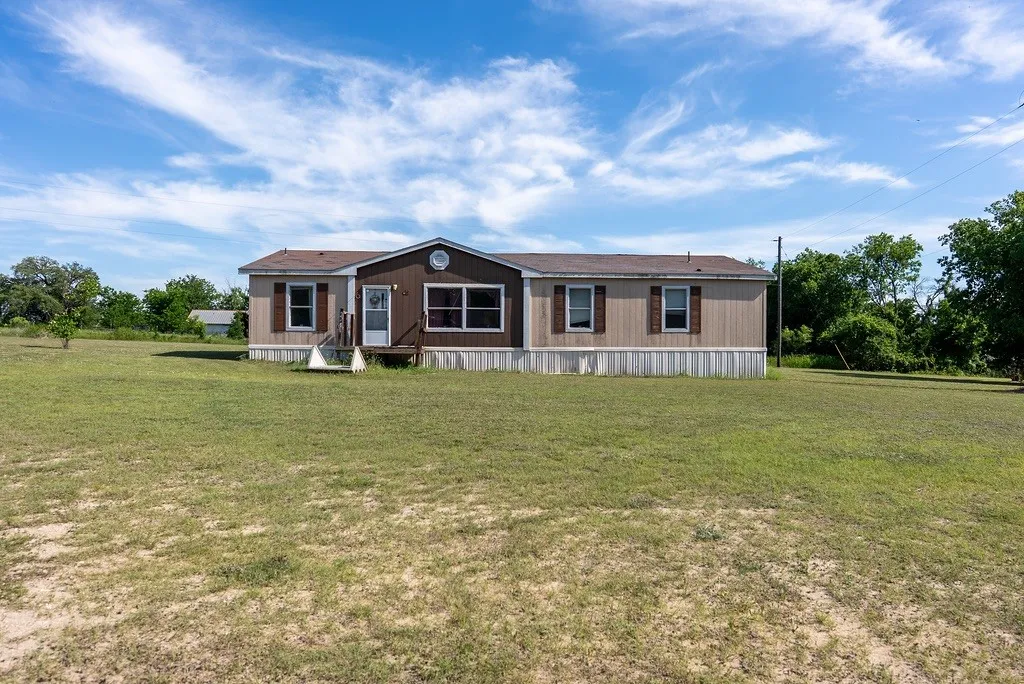 SECONDARY MOBILE HOME- Single-story property featuring a front porch with steps, an exterior with light-colored siding and dark brown accents, and a brown shingle roof- INTERIOR PICS AVAILABLE BY REQUEST ONLY