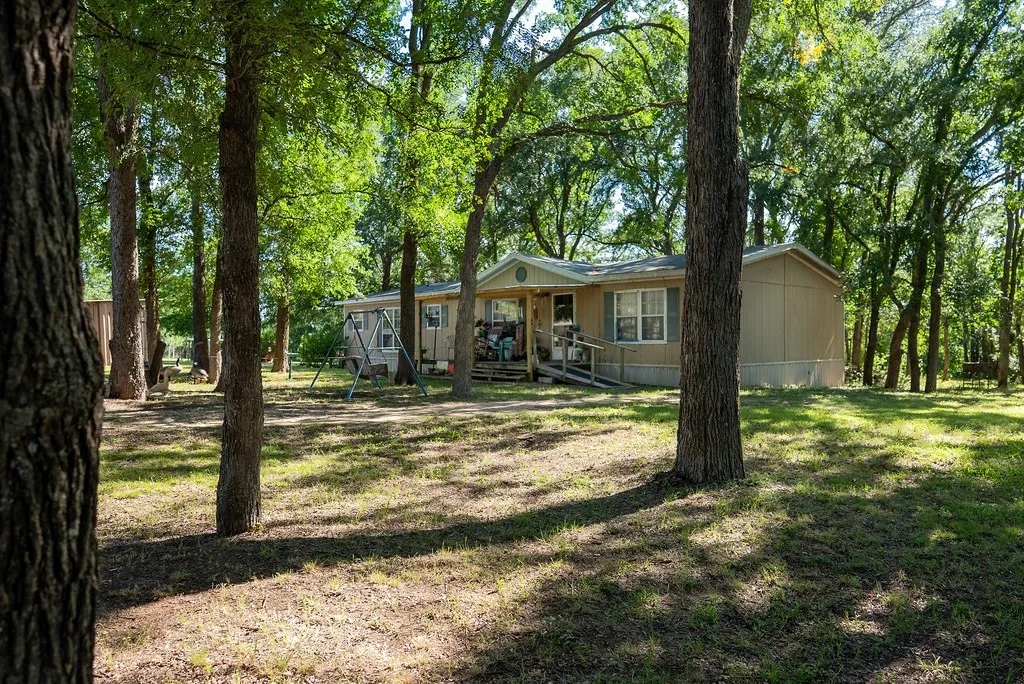 Wooded lot featuring mature trees, a tan siding residence with a covered porch, and a ramp entry