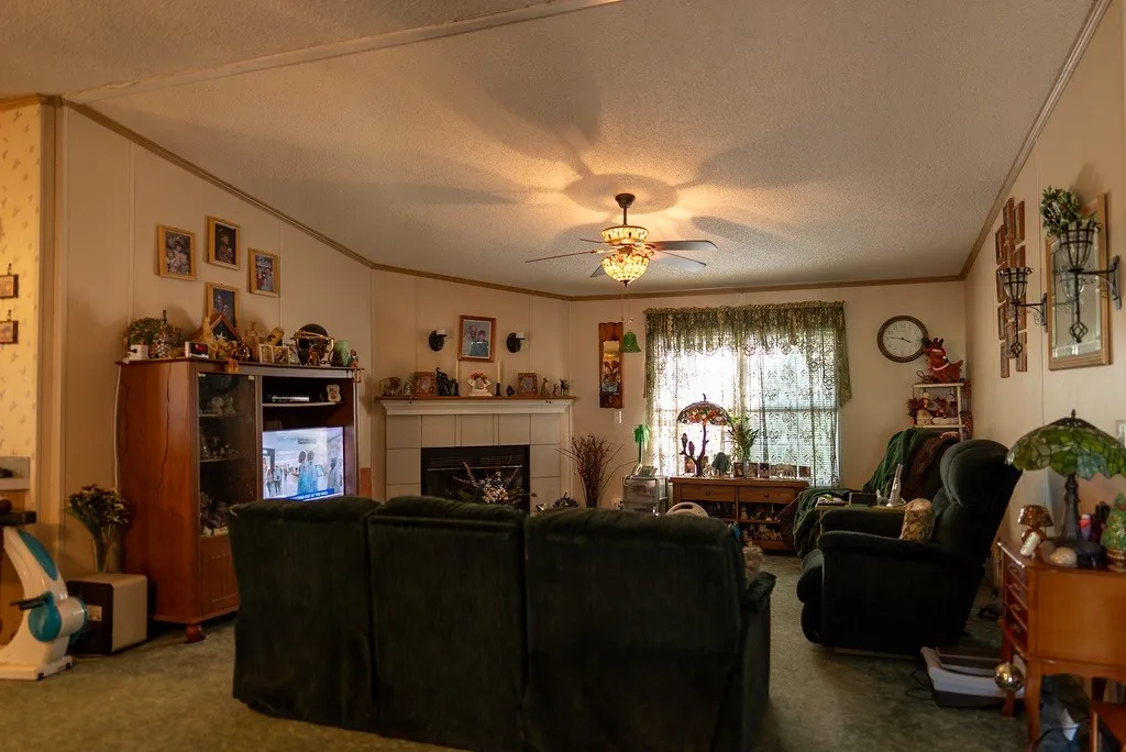 Living area featuring a central ceiling fan with integrated lighting, a fireplace with a mantel, and decorative wall sconces