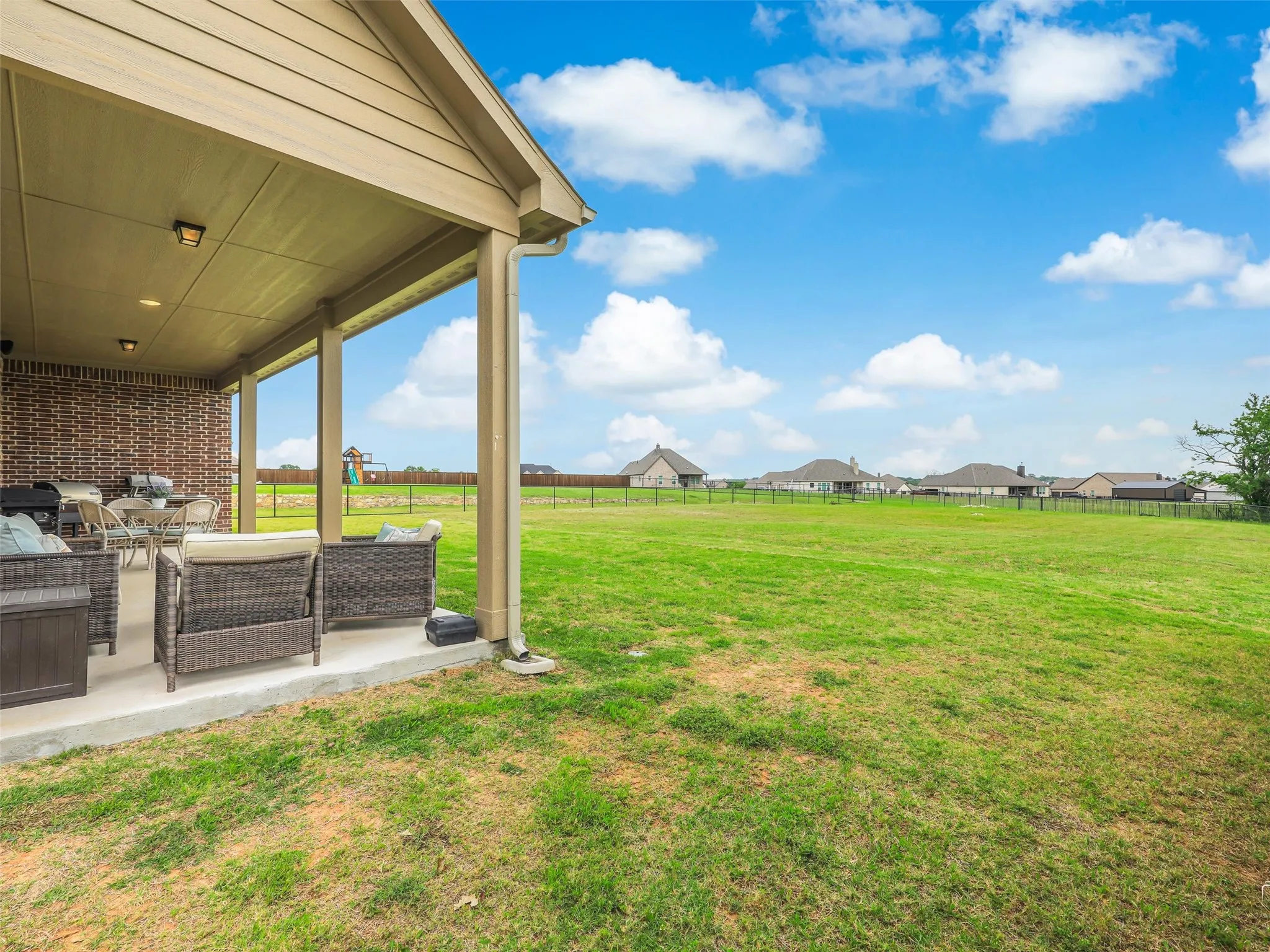 Extended view of the expansive covered back porch at 544 Majors Road, overlooking the sprawling 1-acre pipe-fenced lot with mature trees and plenty of room for a future pool or sports court in Van Alstyne, TX.