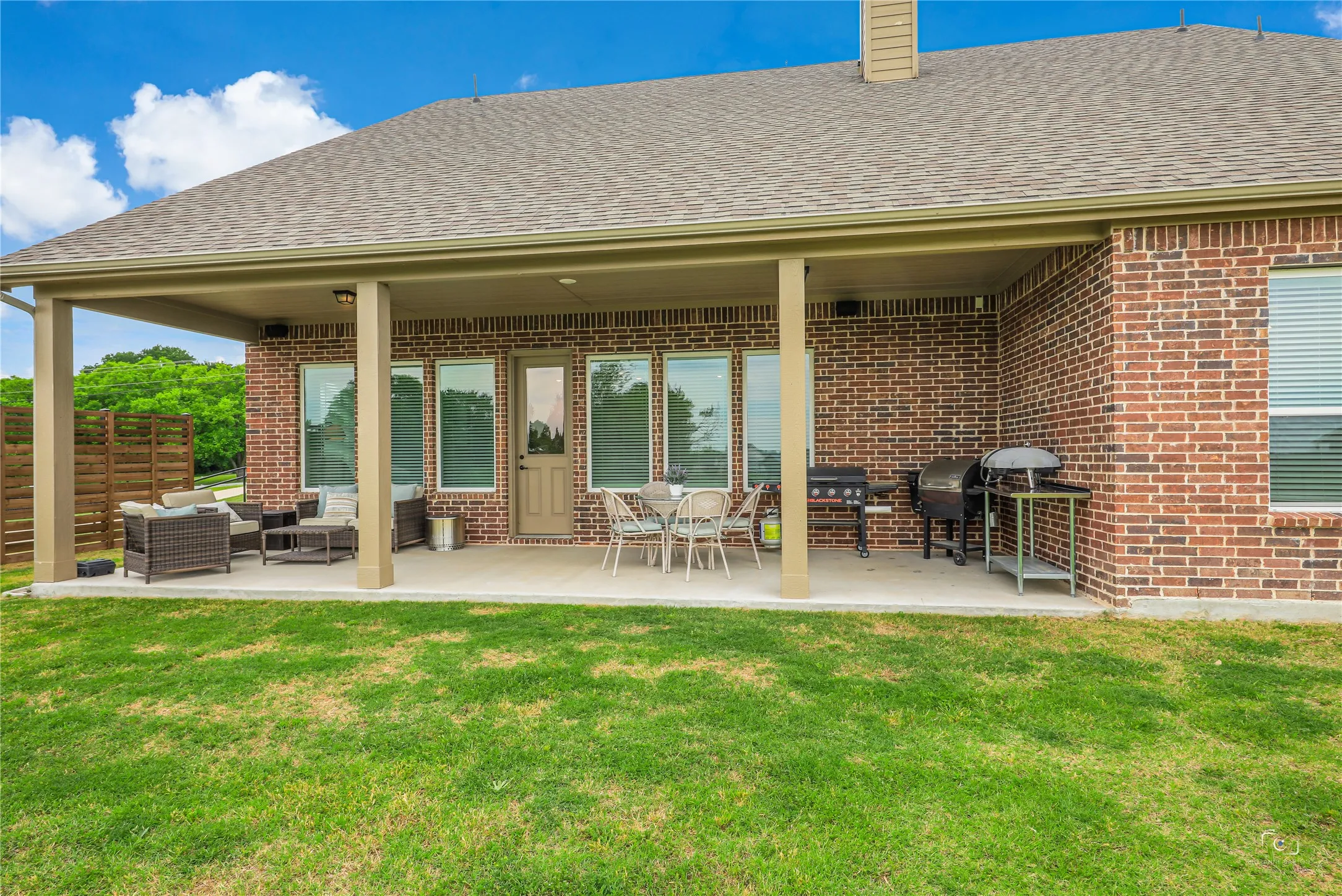 Expansive covered patio featuring a concrete surface, brick exterior, multiple windows, and a privacy screen