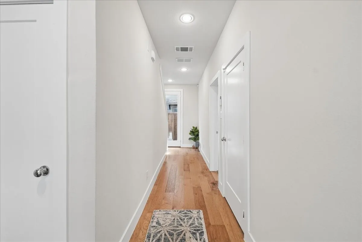 Bright hallway featuring wood-finish flooring, recessed lighting, white walls, and multiple panel doors