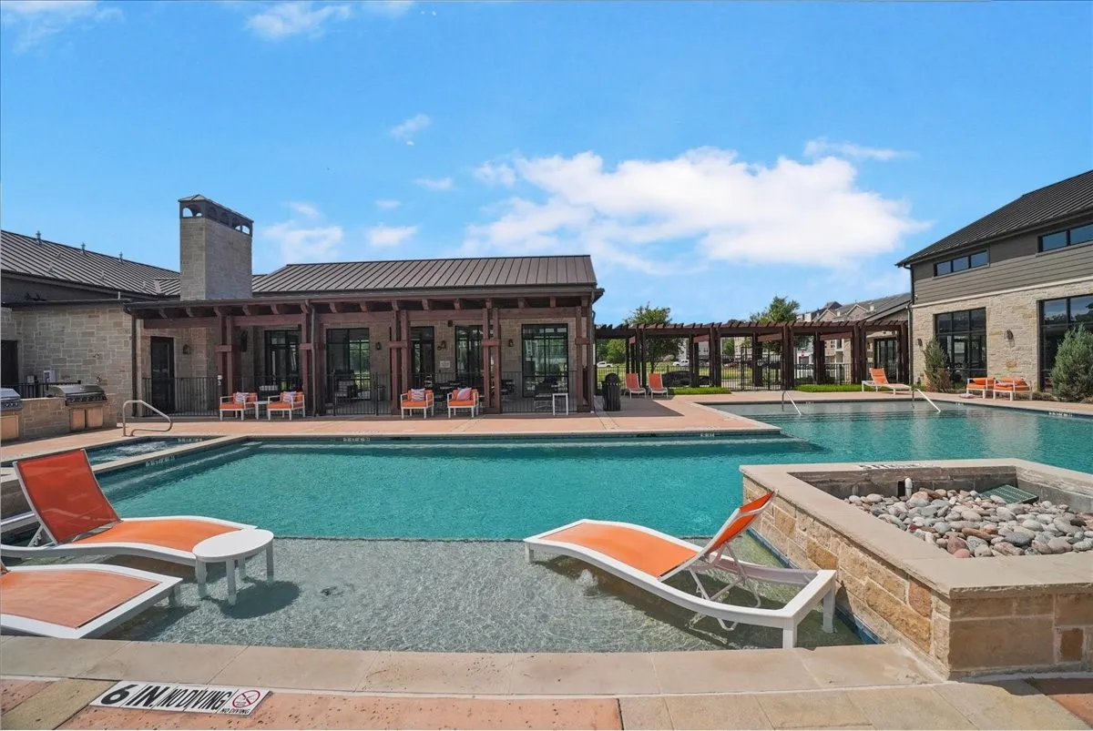 Resort-style swimming pool featuring a tanning ledge, integrated spa, and adjacent stone fire pit