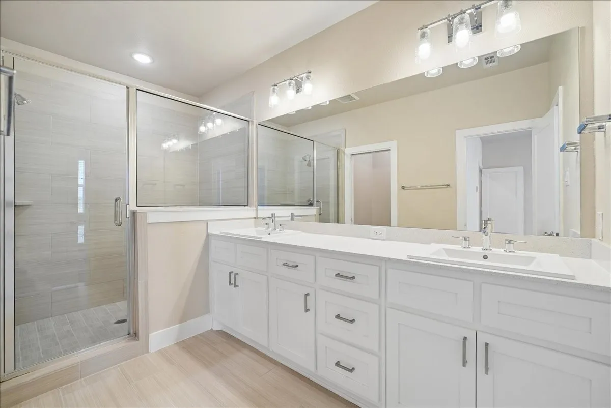 Spacious bathroom featuring a frameless glass shower enclosure, dual vanity with undermount sinks, stone-finish countertops, extensive mirror, and recessed lighting