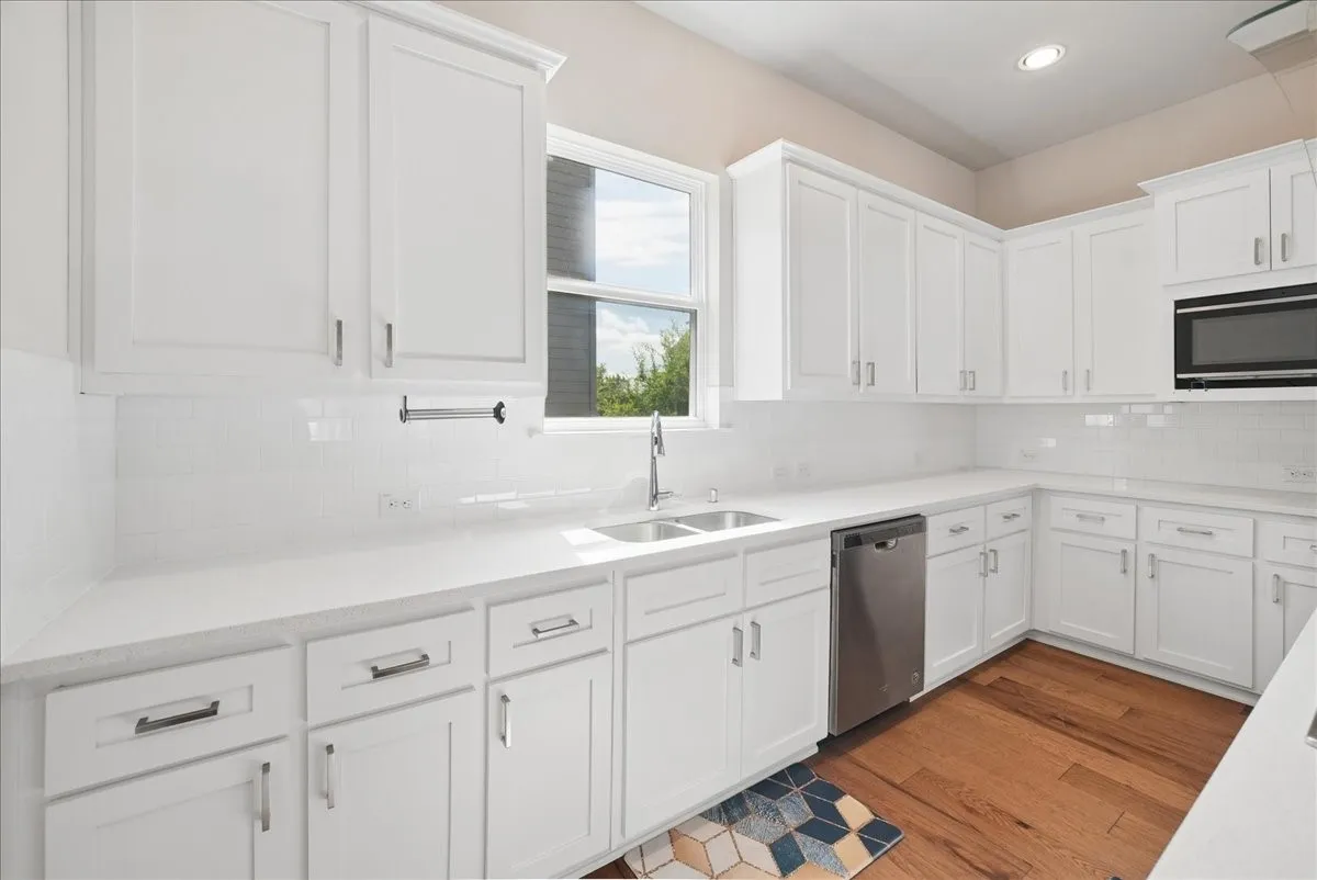 Bright kitchen featuring white shaker-style cabinetry, white subway tile backsplash, white countertops, stainless steel undermount sink, and wood-finish flooring