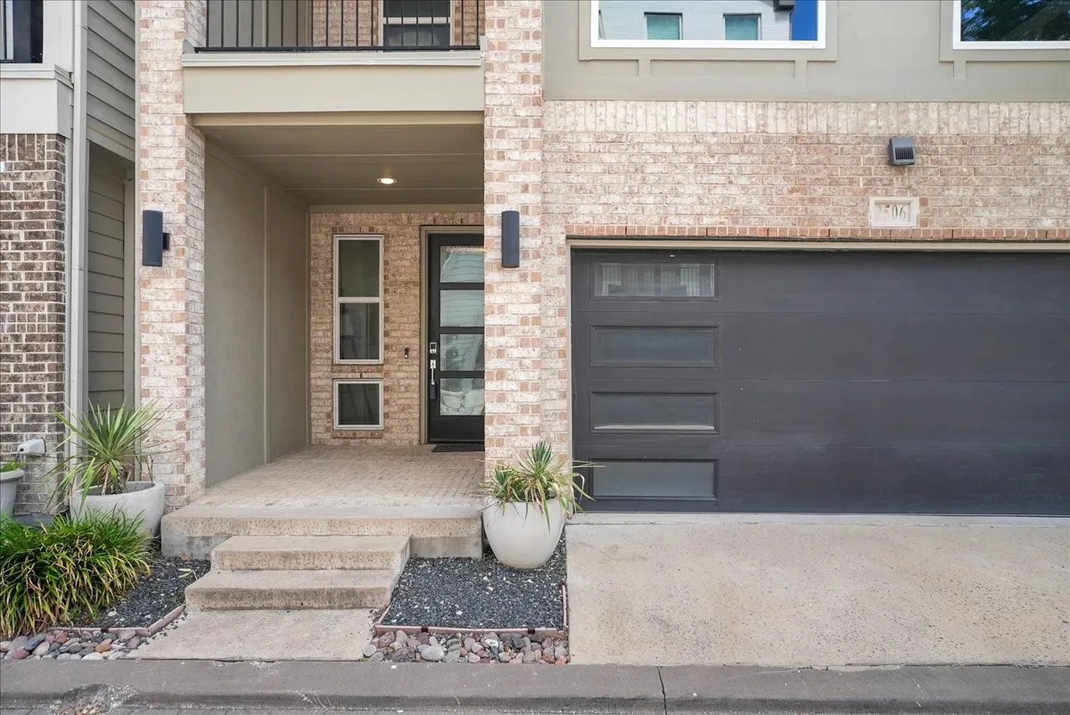 Brick exterior featuring a modern garage door with rectangular window inserts, a recessed entry with a dark door, contemporary exterior lighting, and a concrete driveway