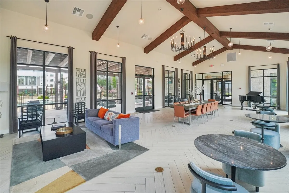 Expansive common area featuring vaulted ceilings with exposed wood beams, light-finish flooring, and multiple glass-paned doors and windows