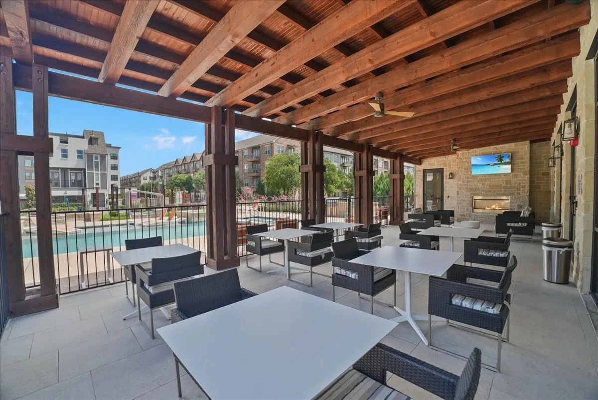 Outdoor covered patio featuring a wood-beam ceiling, stone accent wall, ceiling fans, and a built-in fireplace