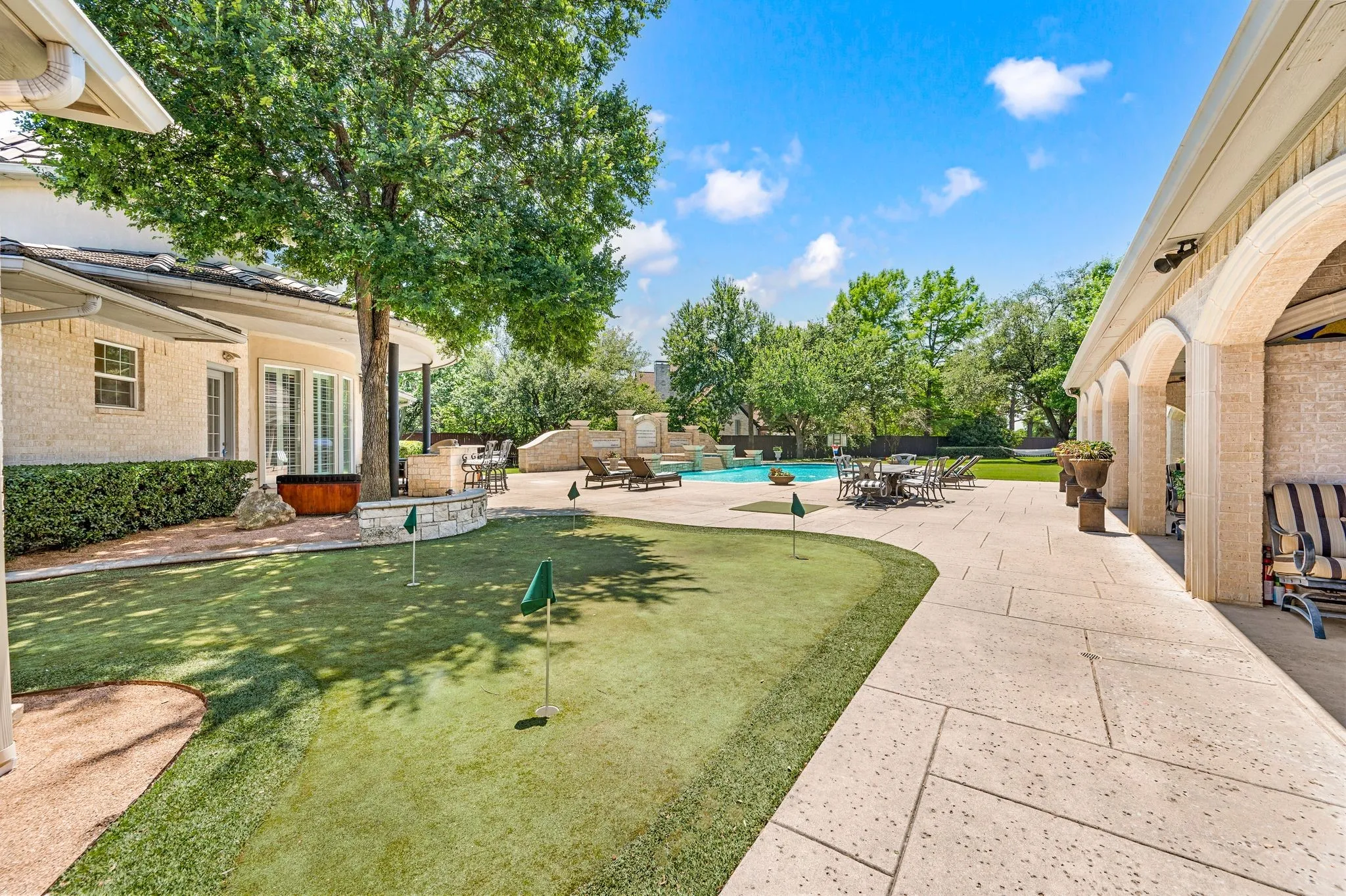 Outdoor putting green with multiple holes, expansive stone patio, arched loggia, built-in swimming pool with waterfall feature, and mature trees