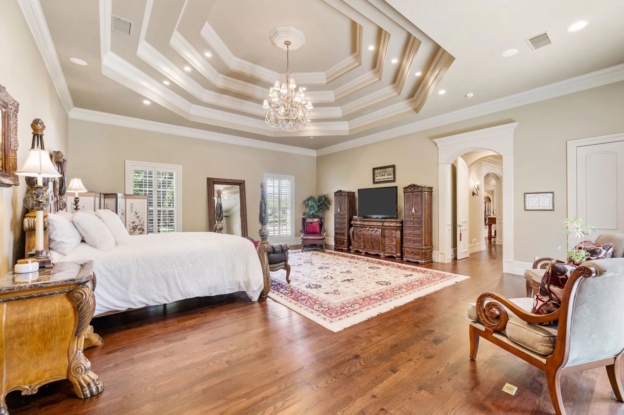 Hardwood flooring throughout featuring a multi-tiered tray ceiling with recessed lighting and a central chandelier