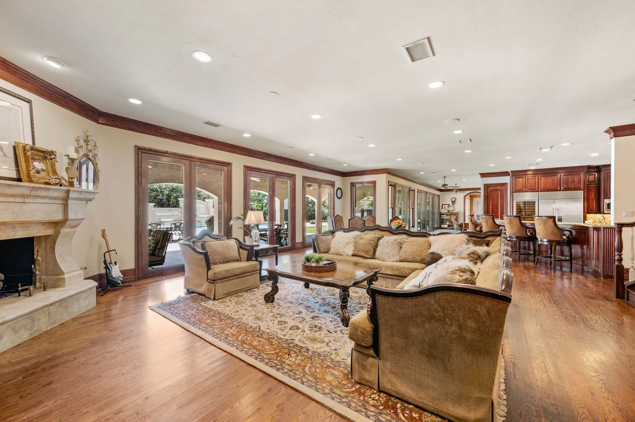 Spacious living area featuring wood-finish flooring, a stone fireplace, and extensive crown molding