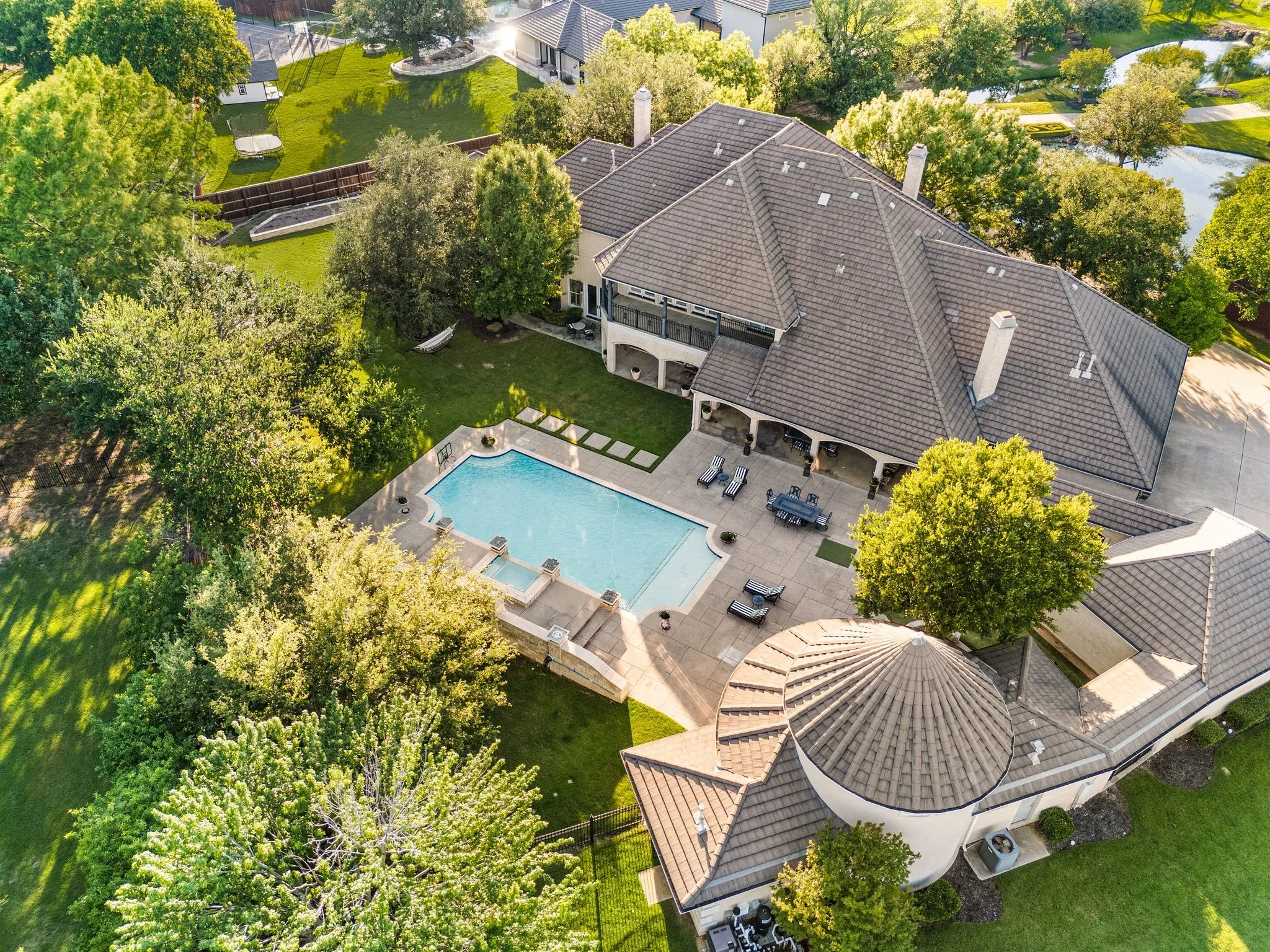 Expansive property featuring a multi-level home with a tiled roof, a large swimming pool with an integrated spa, extensive hardscaping, and mature trees