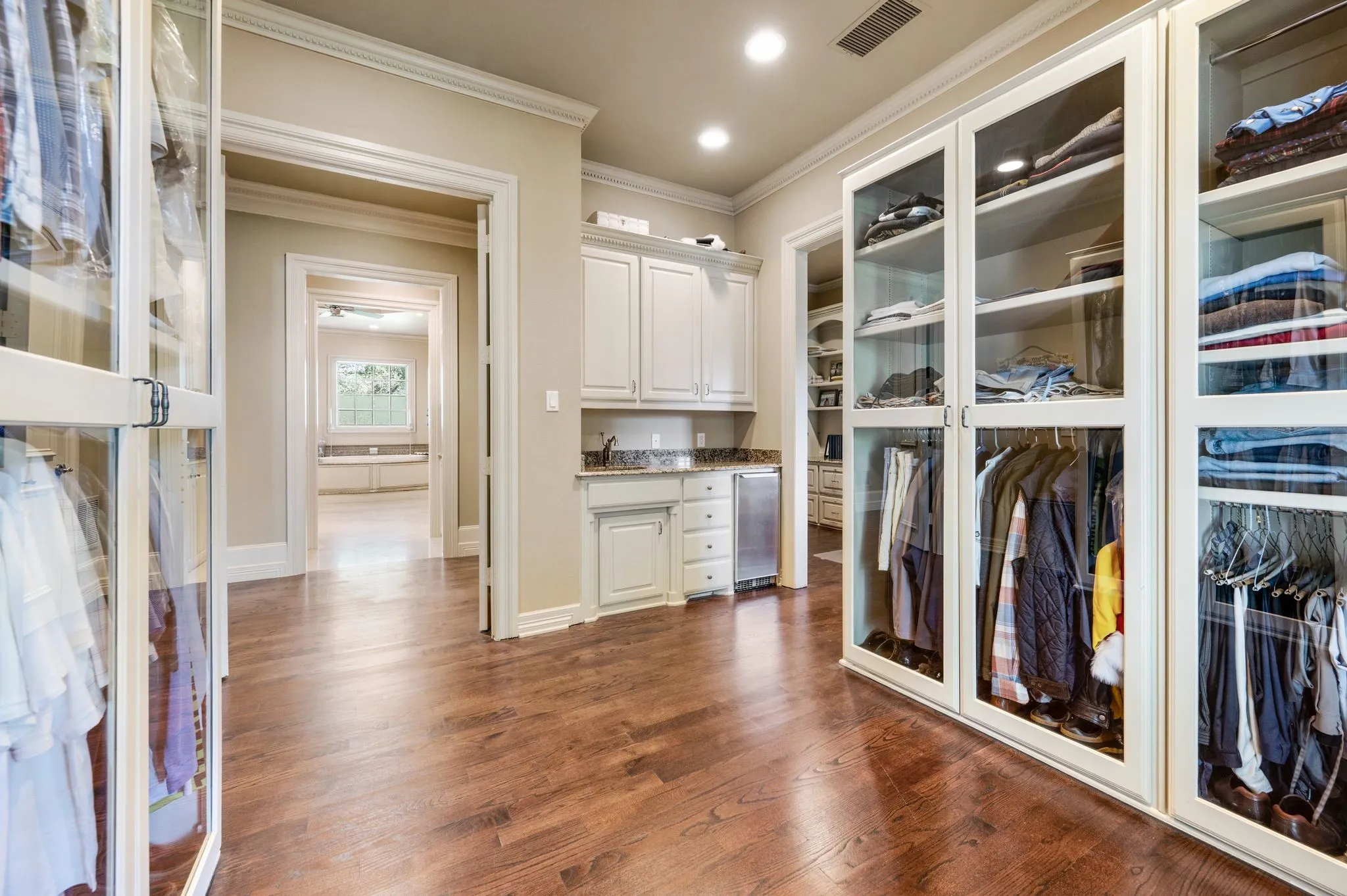Custom closet system featuring glass-front cabinetry, wood-finish flooring, recessed lighting, and crown molding