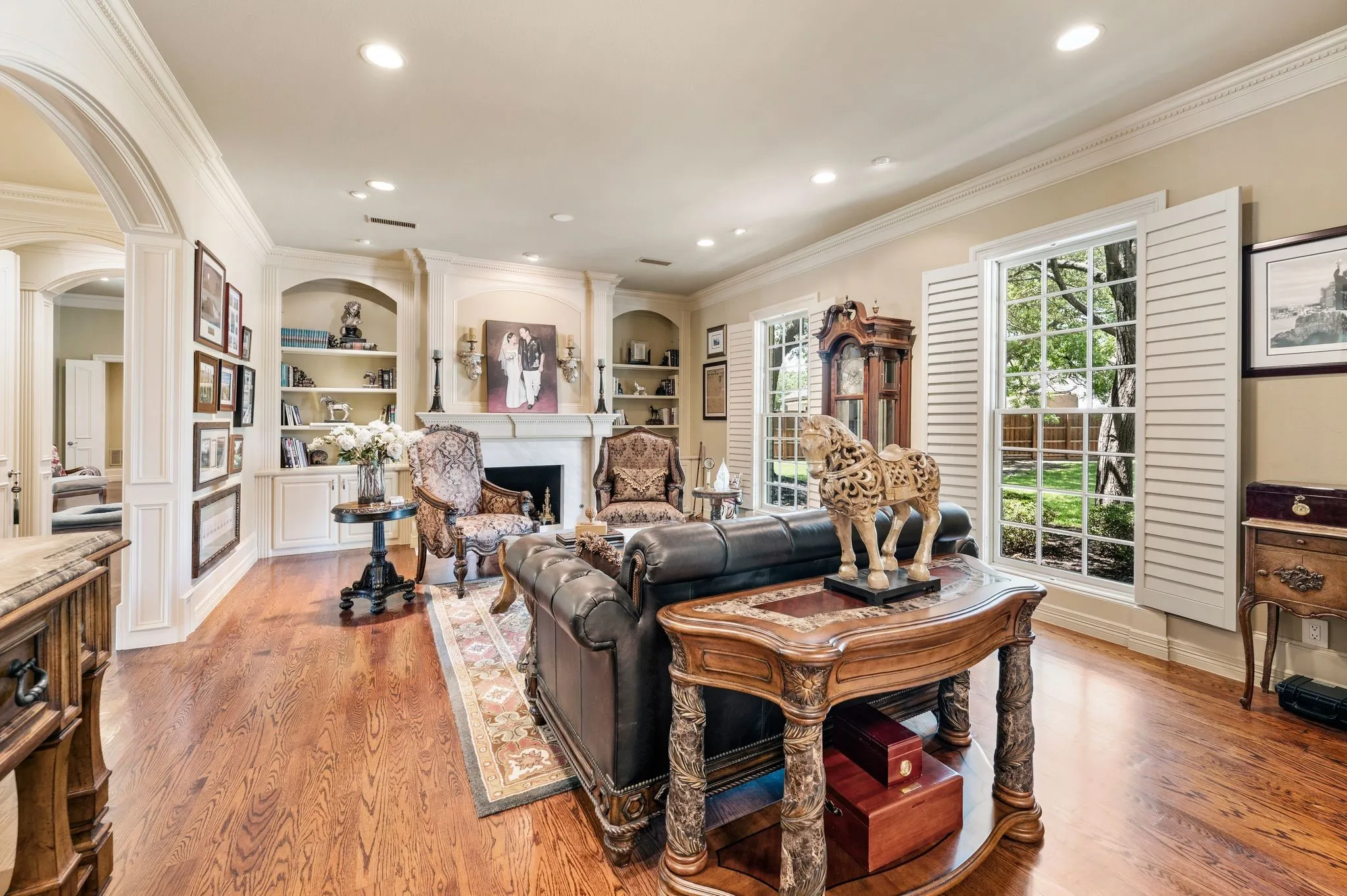 Spacious interior featuring wood-finish flooring, a fireplace with a stone surround, built-in shelving, decorative archways, and window shutters