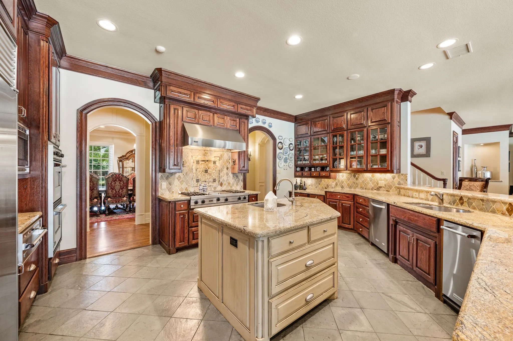 Expansive kitchen featuring a central island, rich wood cabinetry, stainless steel appliances, and stone tile flooring