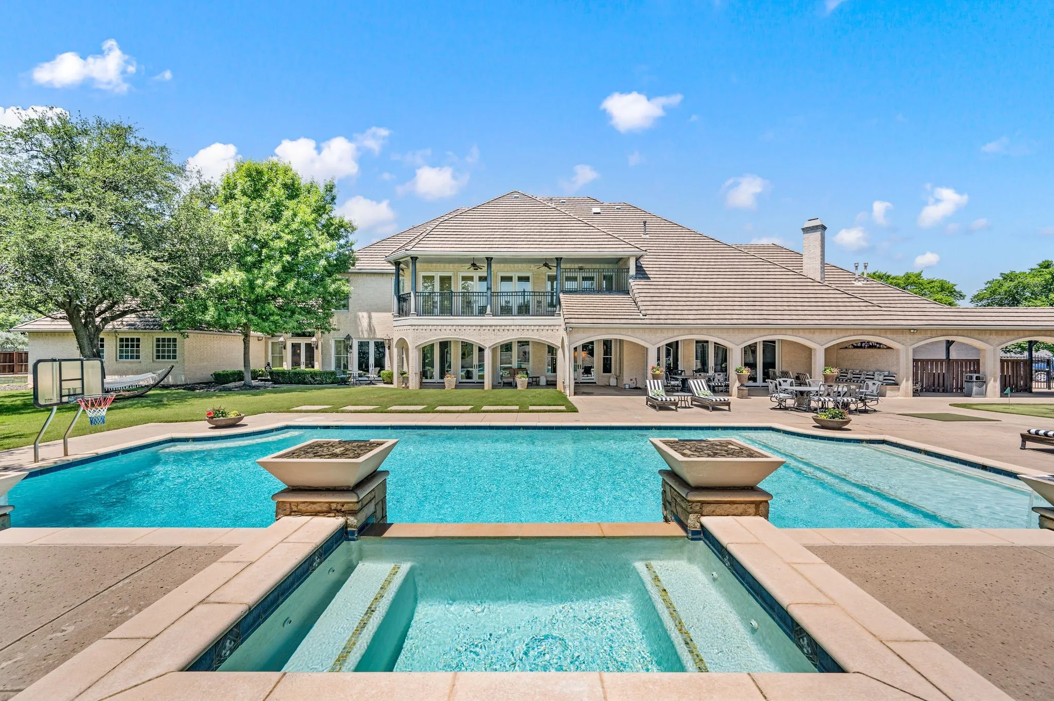 Expansive outdoor living area featuring a large swimming pool with integrated spa, a substantial tiled patio, an arched covered patio, and a second-level balcony
