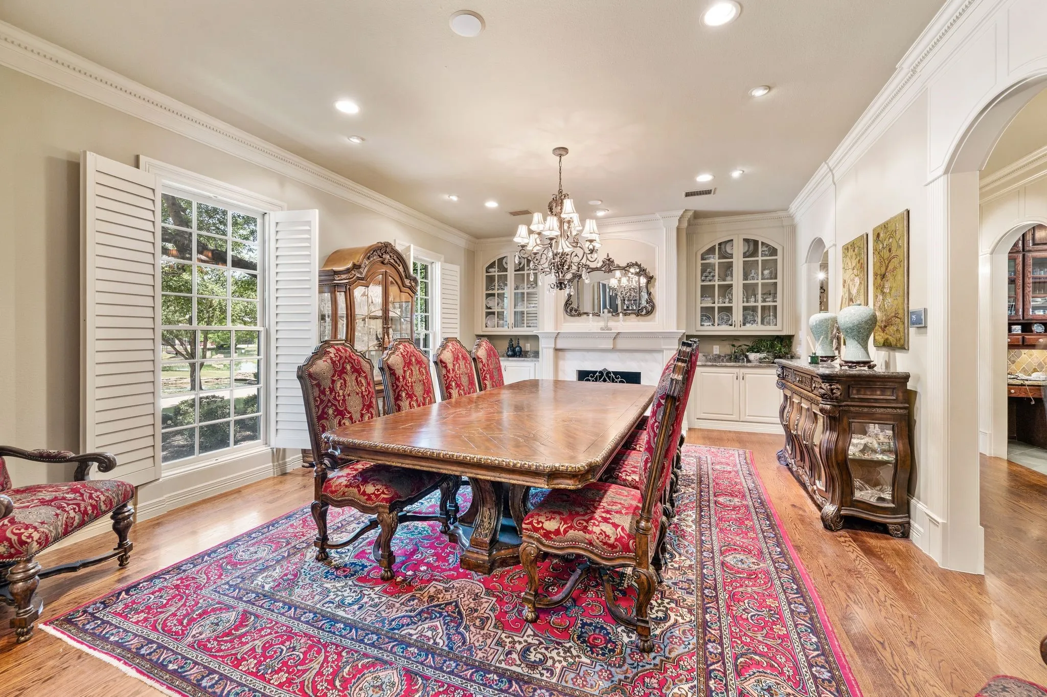 Dining area featuring wood-finish flooring, white plantation shutters, a built-in buffet with glass-front cabinetry, and an arched entry
