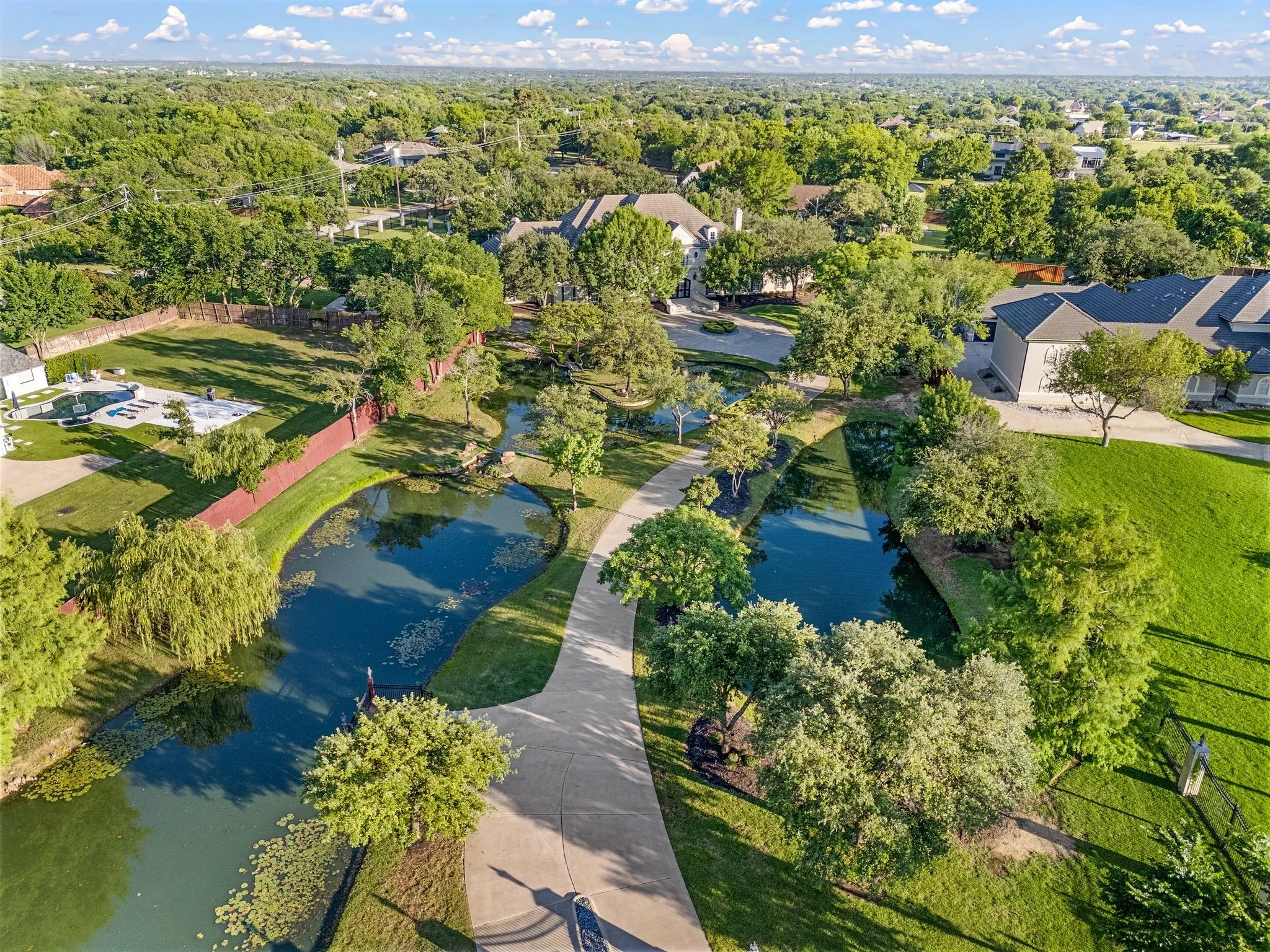 Expansive property featuring a curving paved driveway, two tranquil ponds, and lush green landscaping
