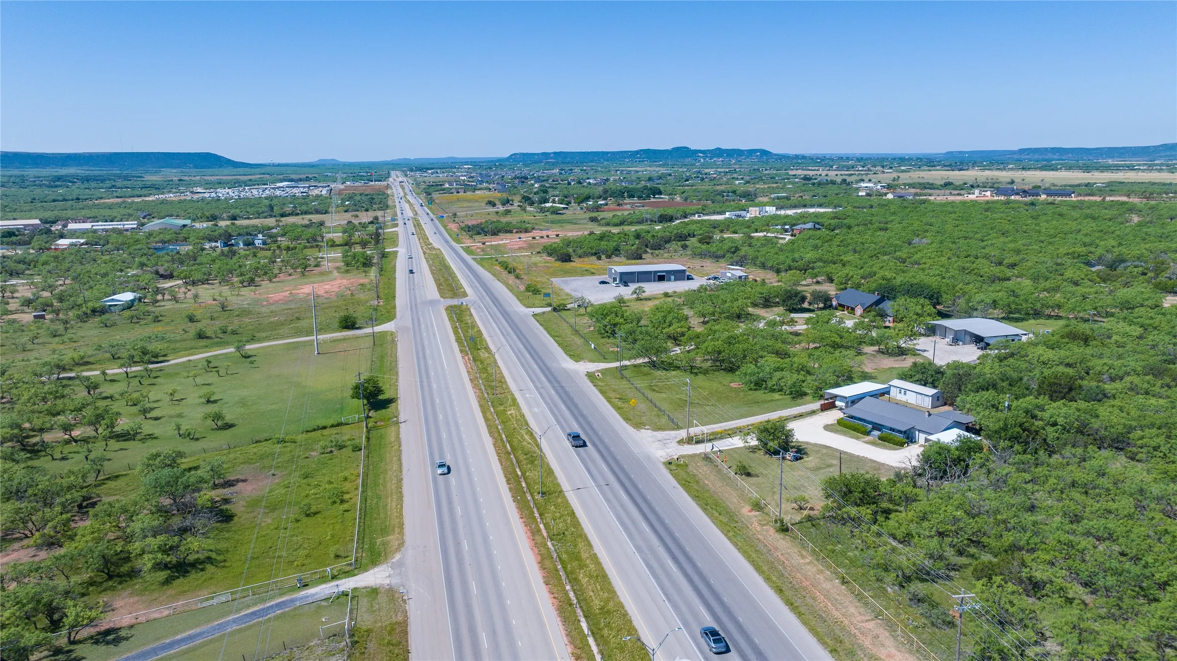 Expansive aerial panorama showcasing a multi-lane highway bordered by greenbelt and scattered structures
