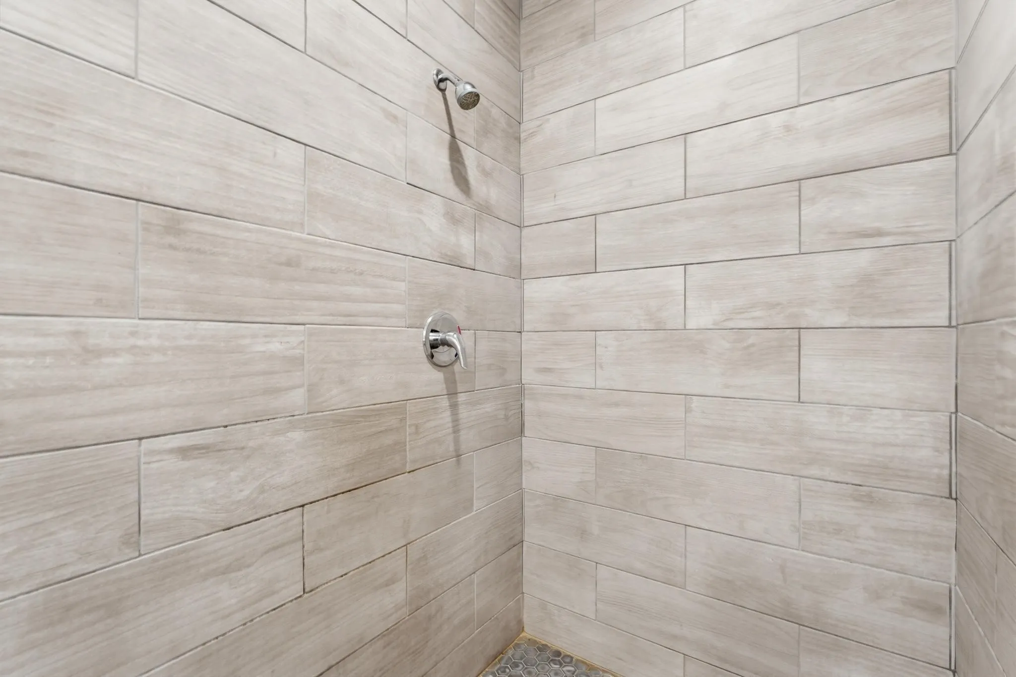 Shower enclosure featuring plank-style wall tiling, a rainfall shower head, and a polished chrome control fixture