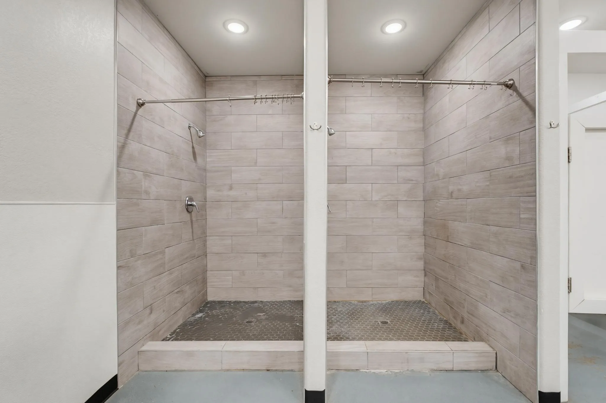 Two tiled shower stalls with recessed lighting, individual showerheads, and textured shower pan flooring