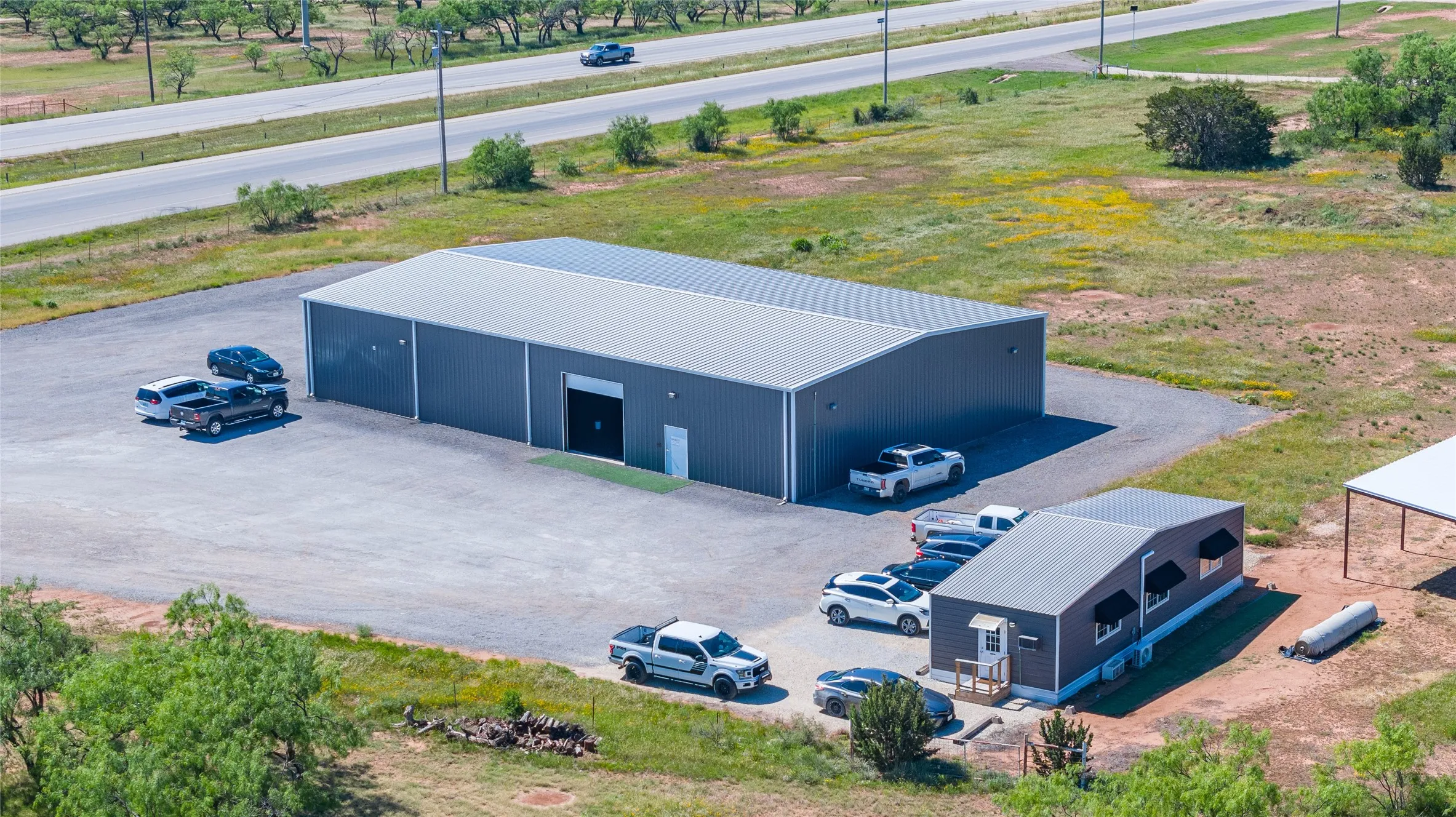 Industrial property featuring a large gray metal building with a white door and a secondary smaller structure with black window awnings