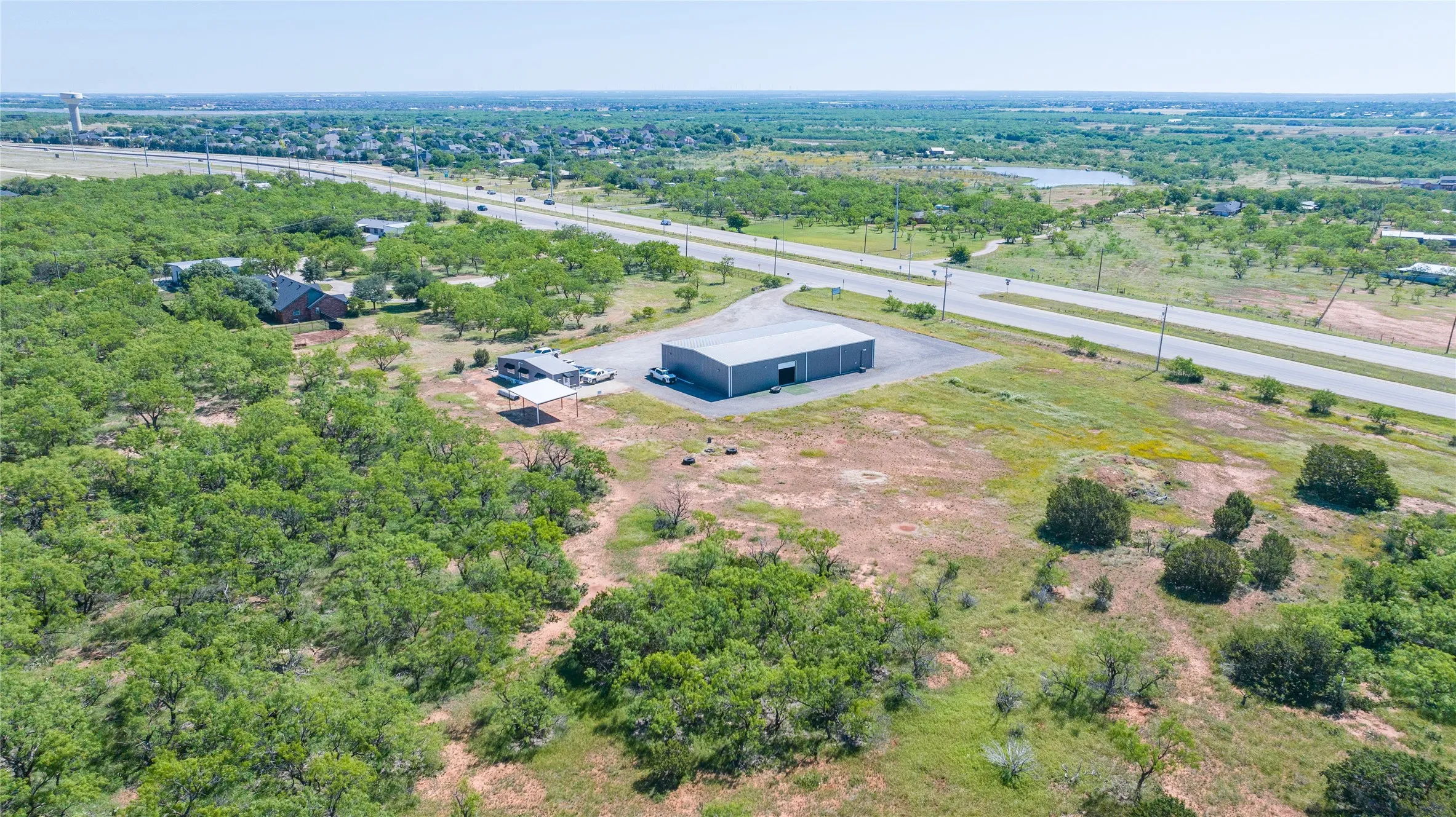 Expansive property featuring a large gray industrial building, a paved driveway, and varied terrain with green foliage