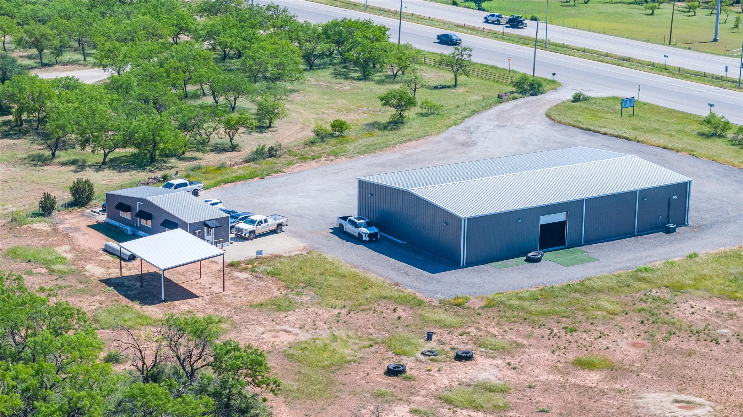 Commercial property featuring a large gray metal building with a roll-up door, a gravel parking area, and a separate smaller structure with an attached carport
