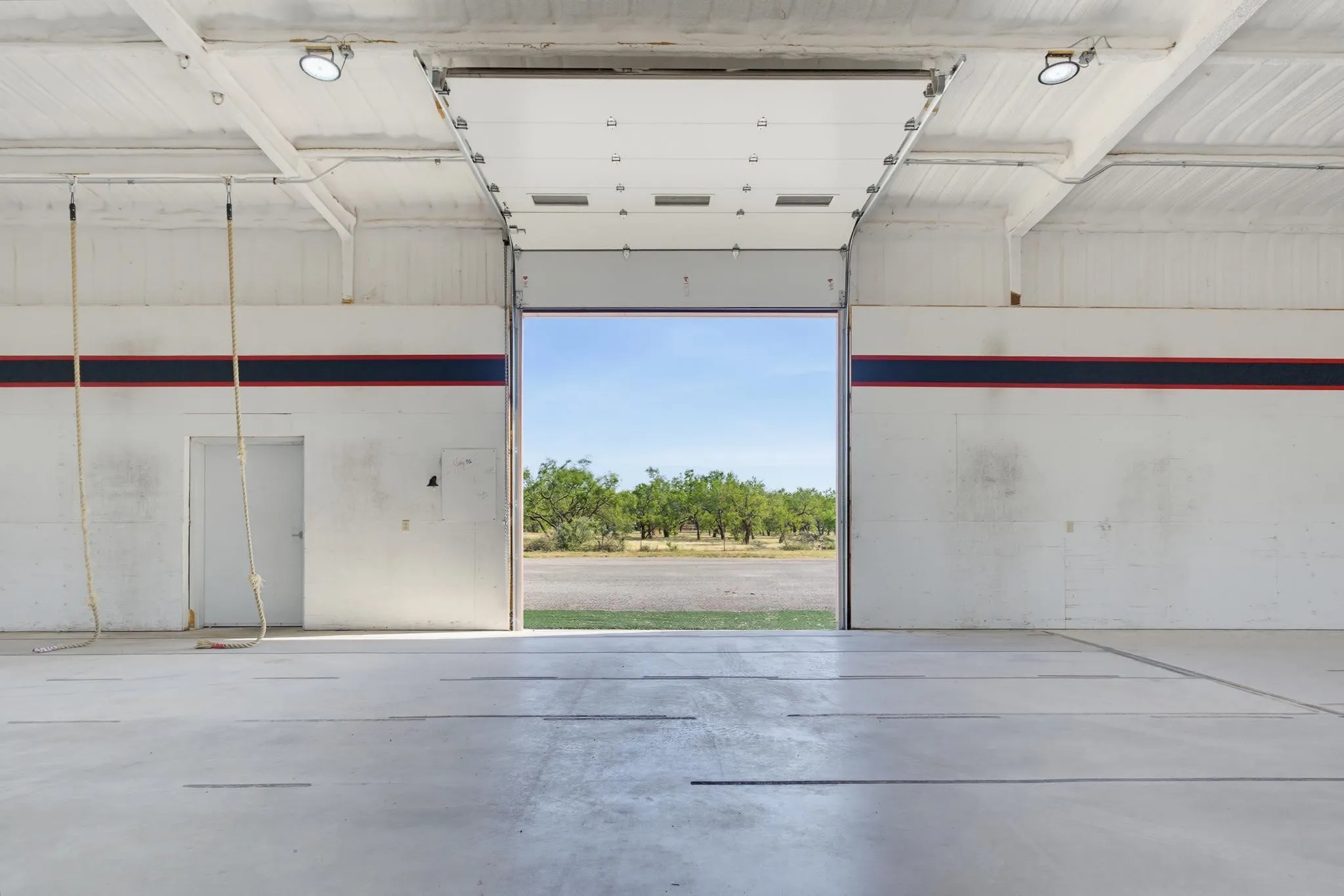 Industrial-style space featuring a large roll-up door, exposed ceiling beams, polished concrete flooring, and flush-mount lighting fixtures