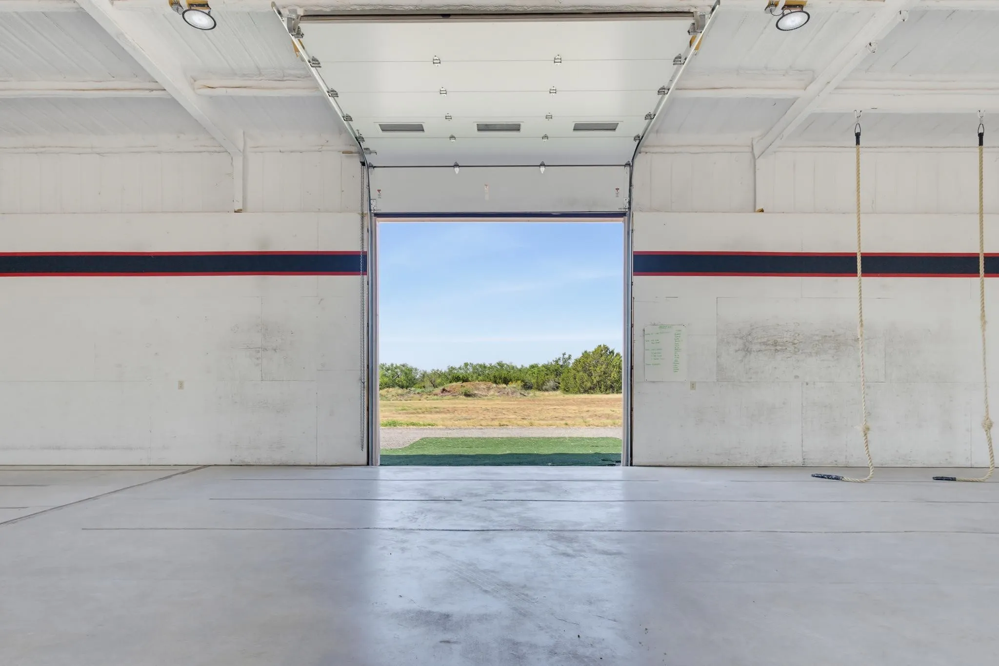 Concrete flooring, overhead lighting, large roll-up door, open ceiling structure, painted interior walls