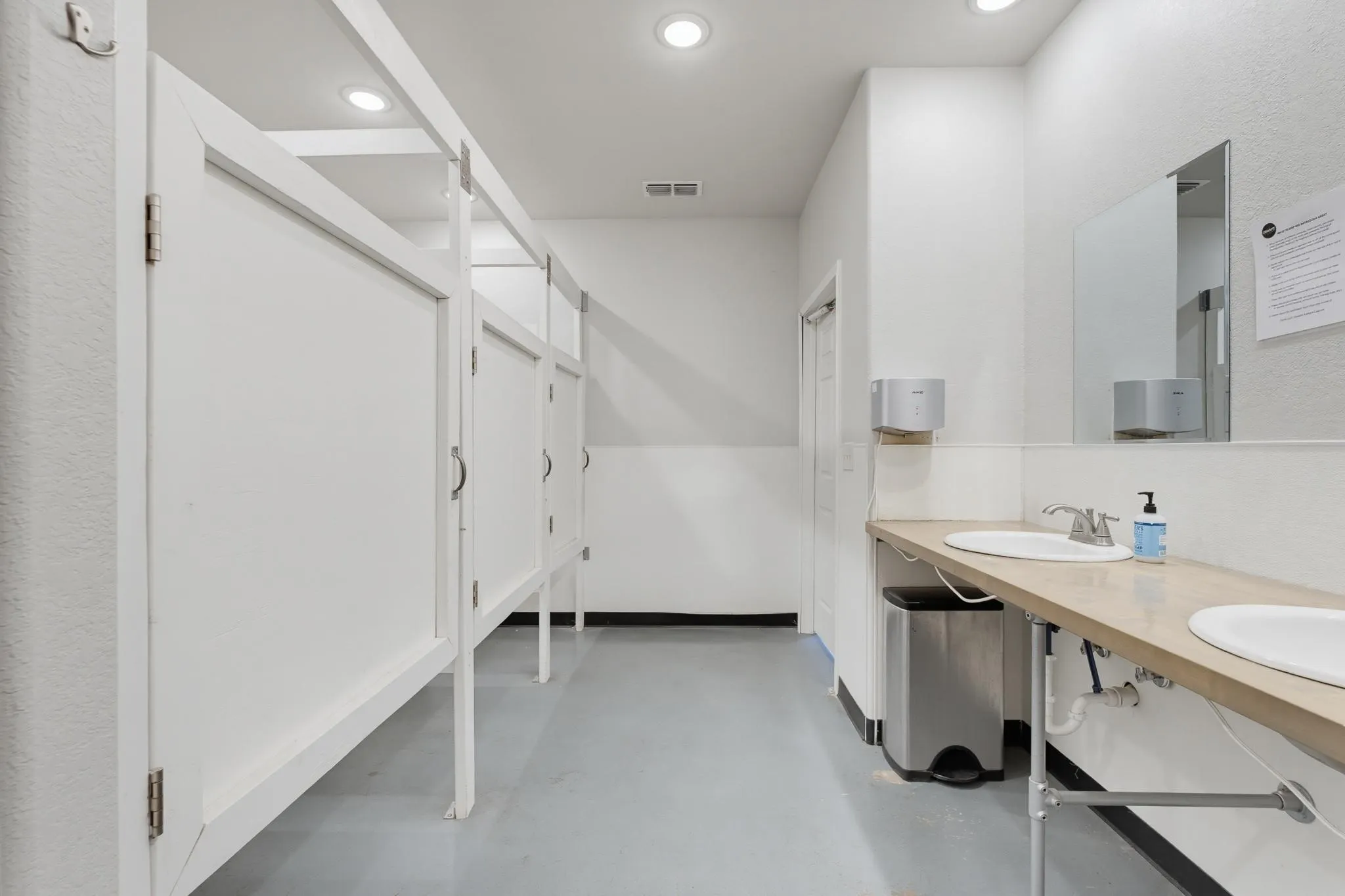 Recessed lighting, light-toned flooring, wall-mounted mirror, dual vanity sinks, and wood-finish countertop