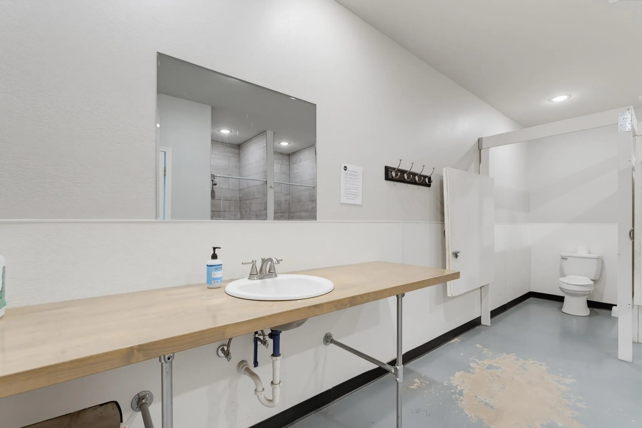 Spacious washroom featuring an extended wood-finish vanity, a contemporary wall mirror, and dedicated stalls with white privacy doors