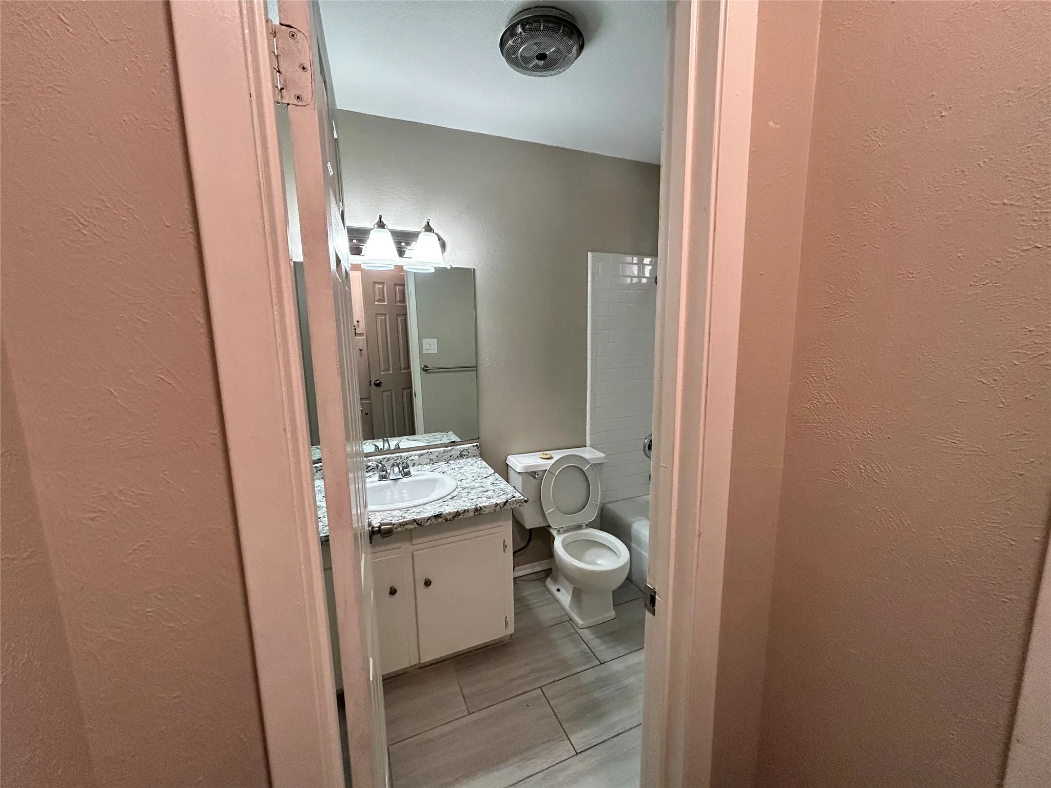 Bathroom featuring a vanity with an integrated sink, a light-toned countertop, white cabinetry, a large wall mirror, and tile flooring