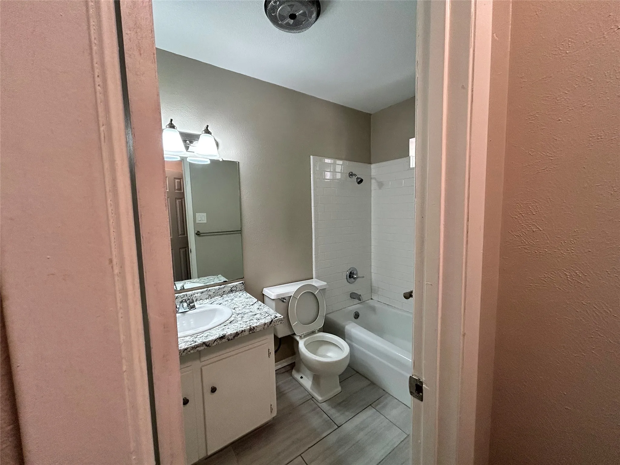 White vanity with a single basin sink, speckled countertop, and wall-mounted mirror