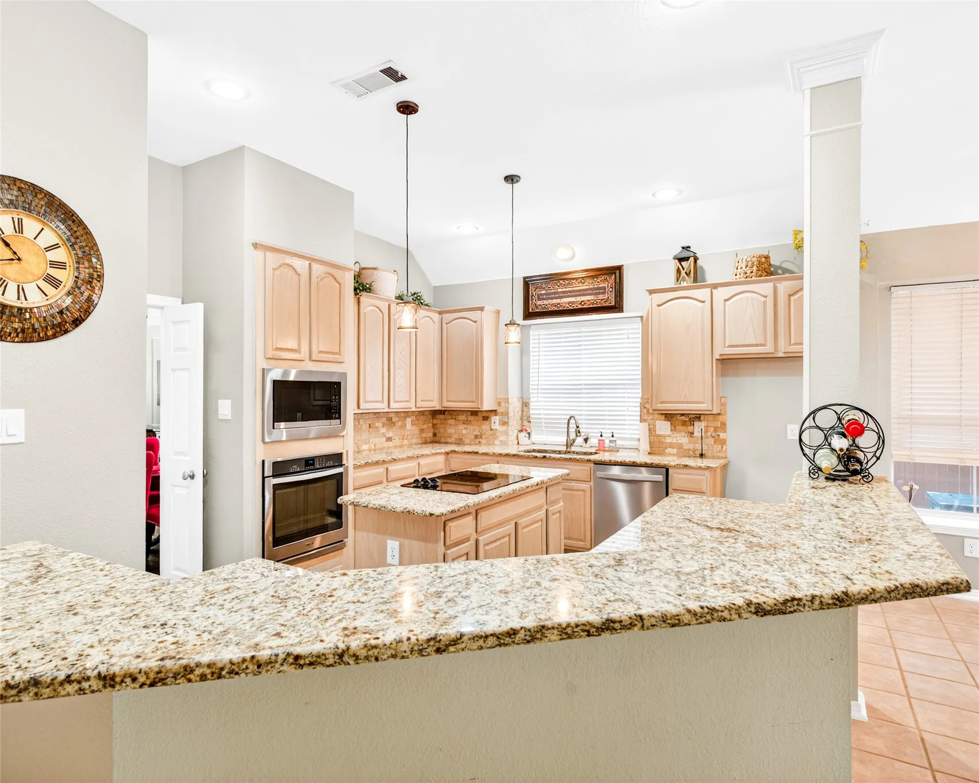 Kitchen featuring light wood cabinetry, stainless steel appliances, and a multi-toned backsplash