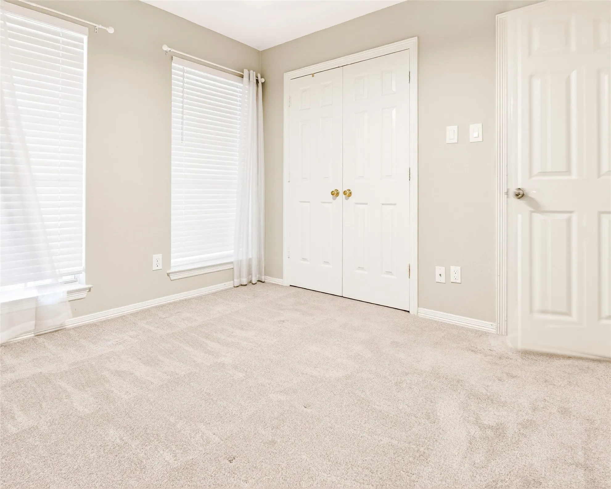Carpeted room featuring two windows with white blinds and sheer curtains, a bifold closet, and a paneled door