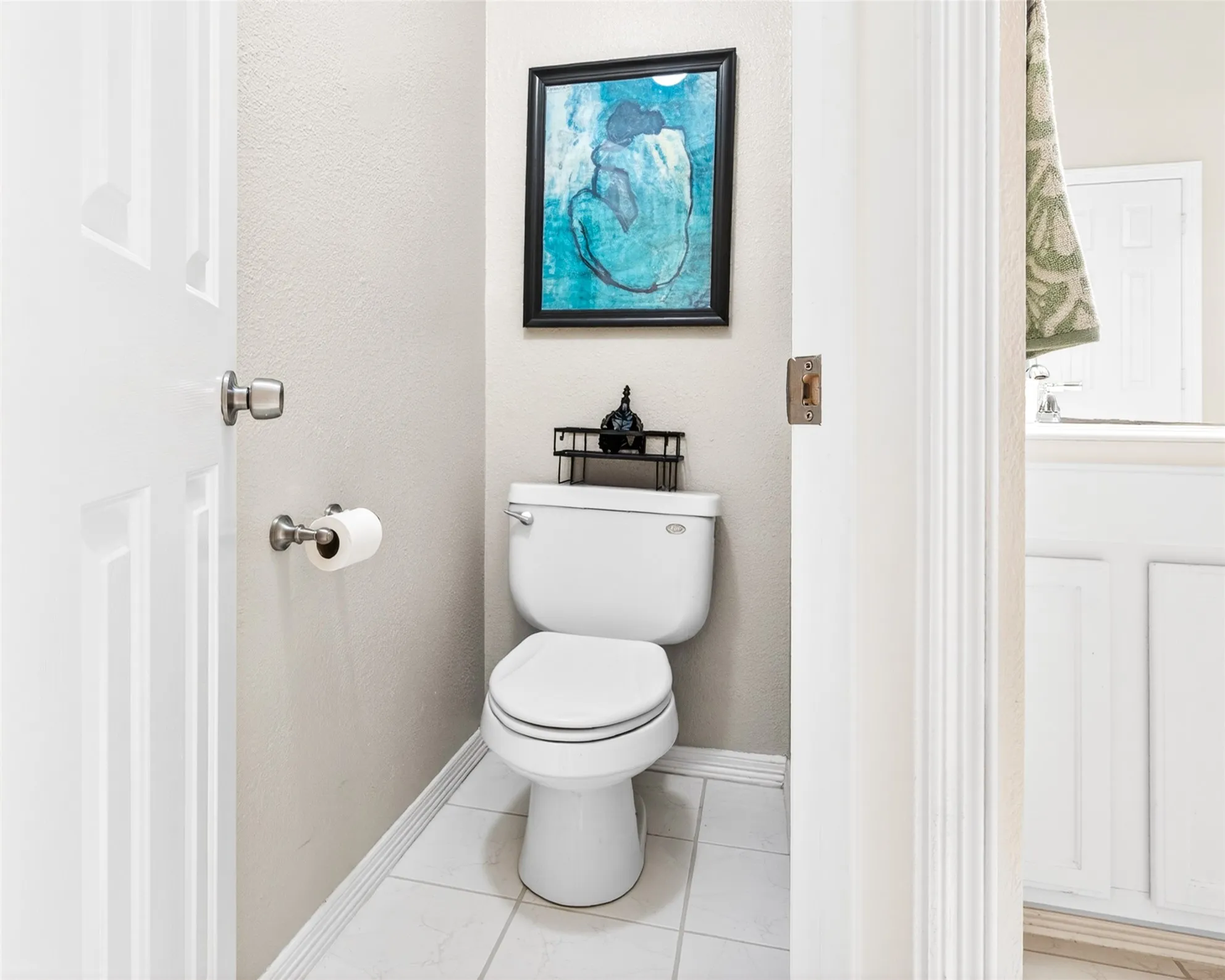 Compact water closet featuring white tile flooring, neutral wall tones, and a white toilet