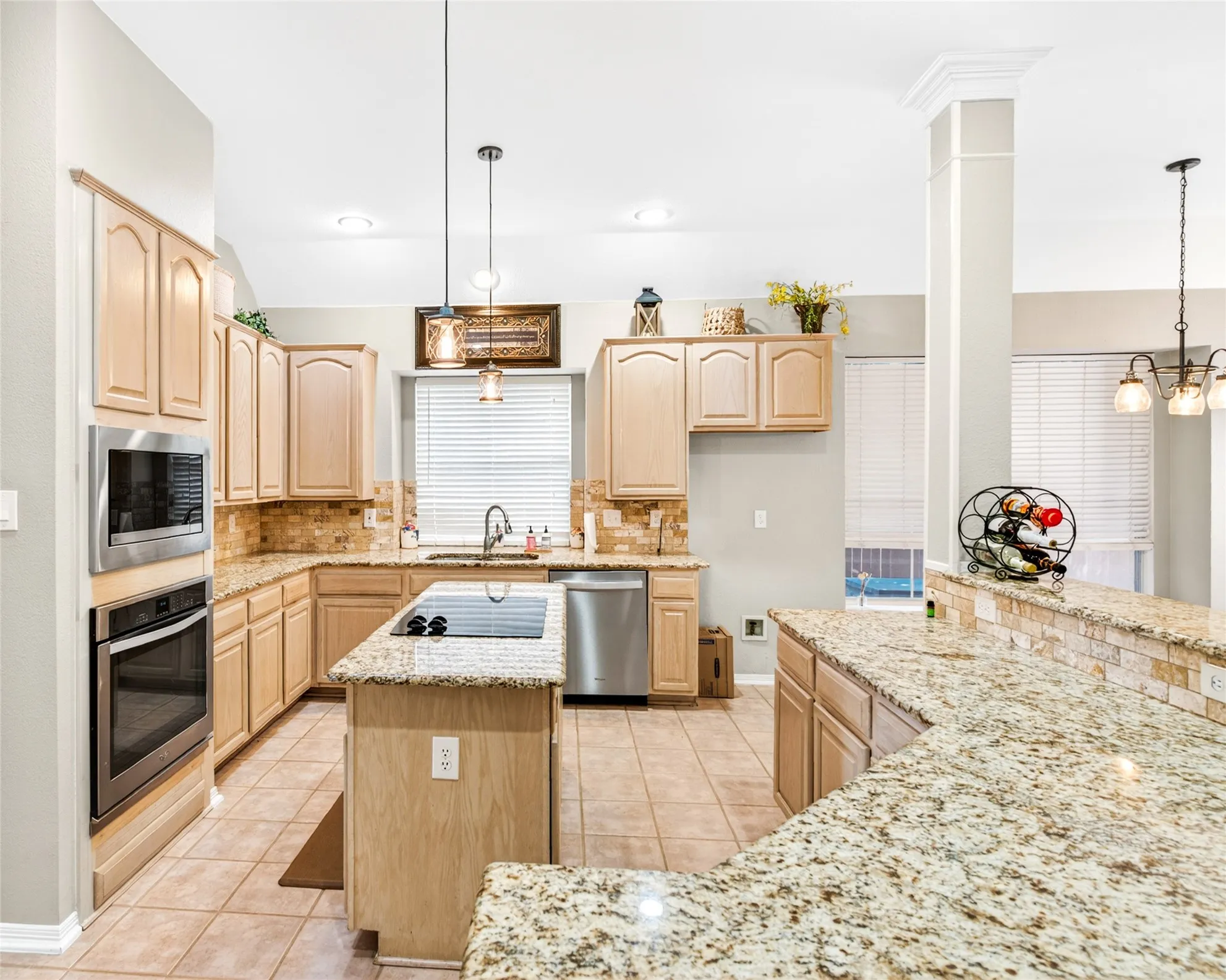 Kitchen featuring granite countertops, light wood-finish cabinetry, stainless steel appliances, a center island with cooktop, and tile flooring