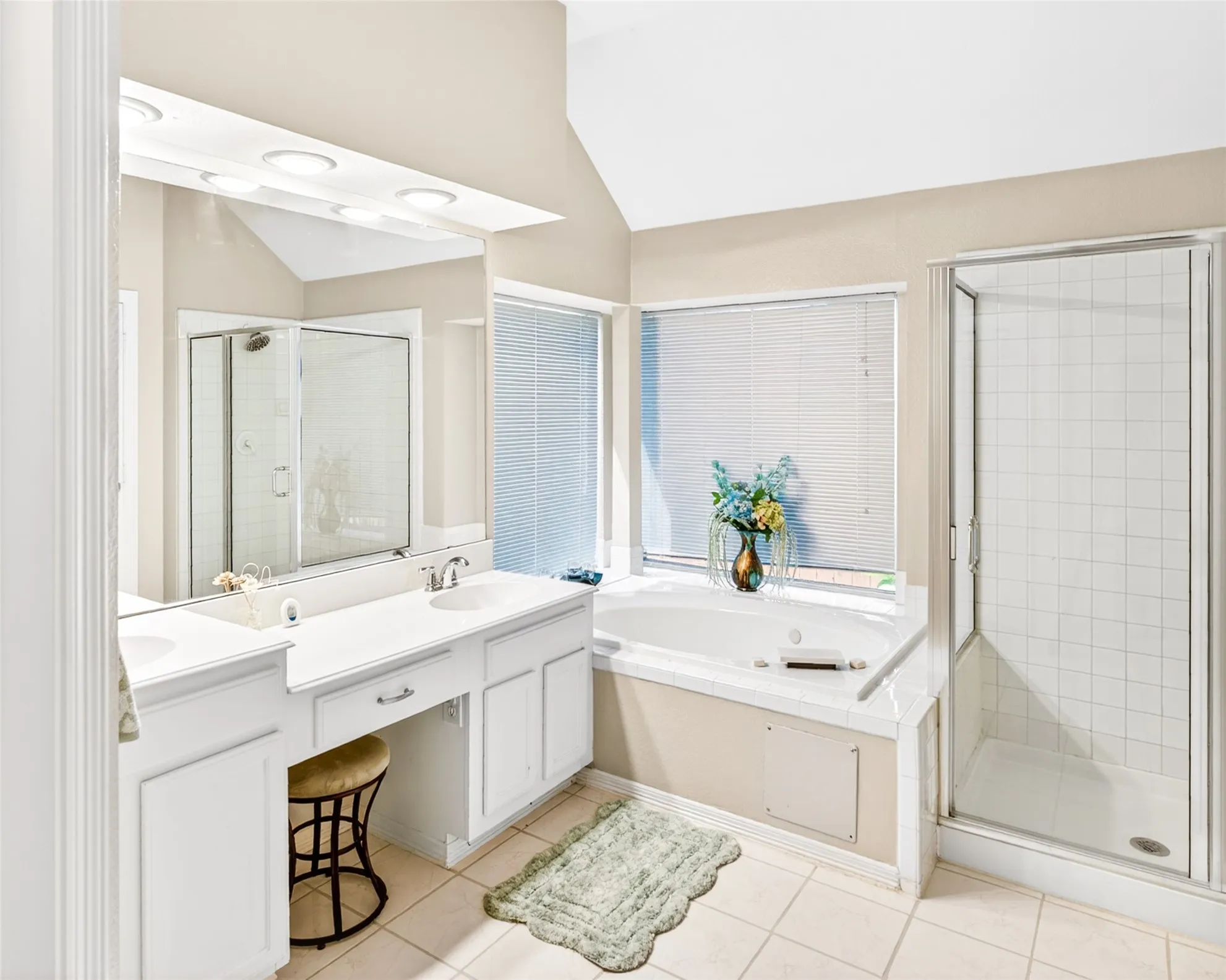 Bathroom featuring a built-in soaking tub, separate glass-enclosed shower, dual vanity with integrated sinks, and ample natural light