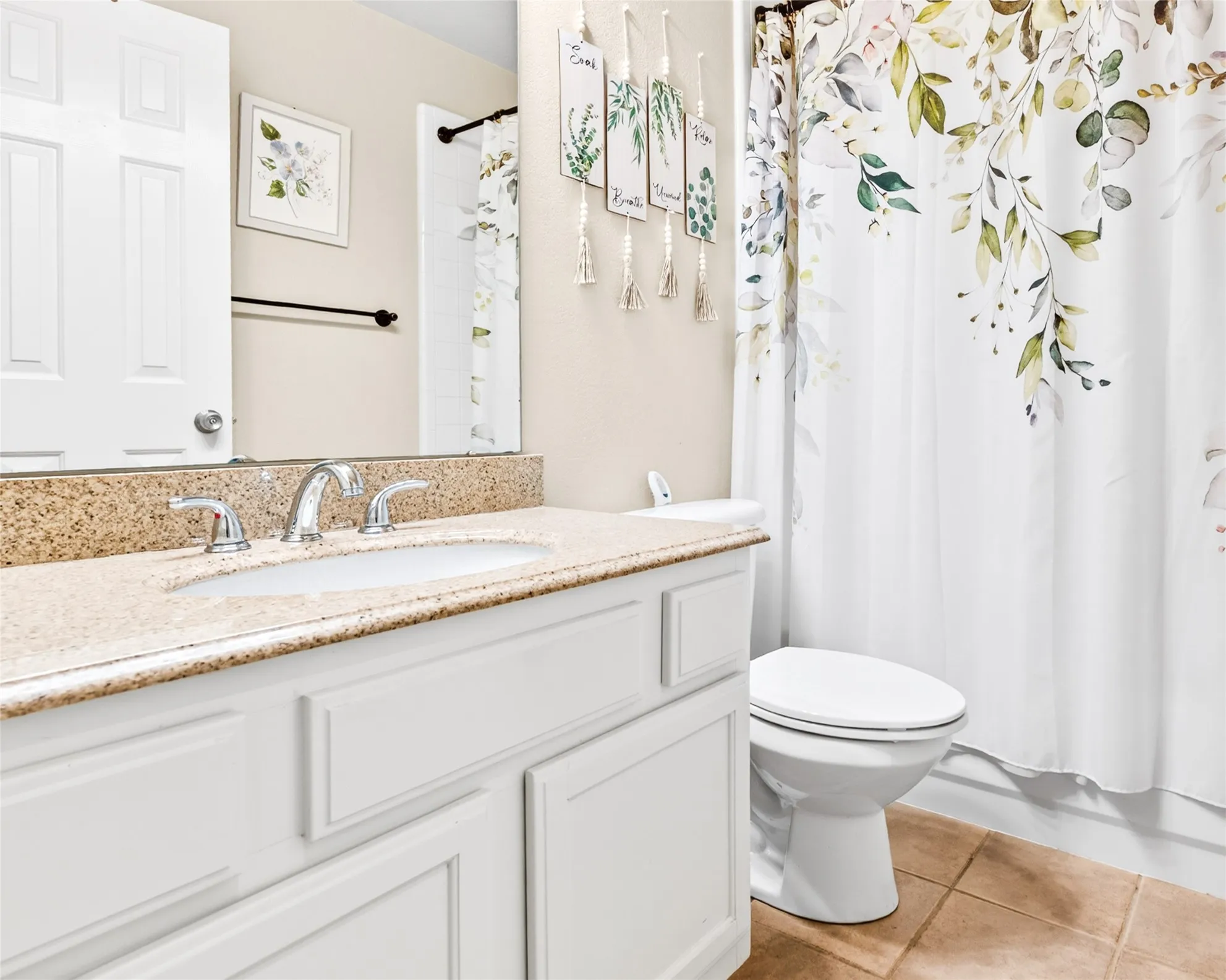 Bathroom featuring a light-colored vanity with panel detailing, a speckled countertop, an undermount sink with a chrome faucet, a white toilet, and neutral floor tiles