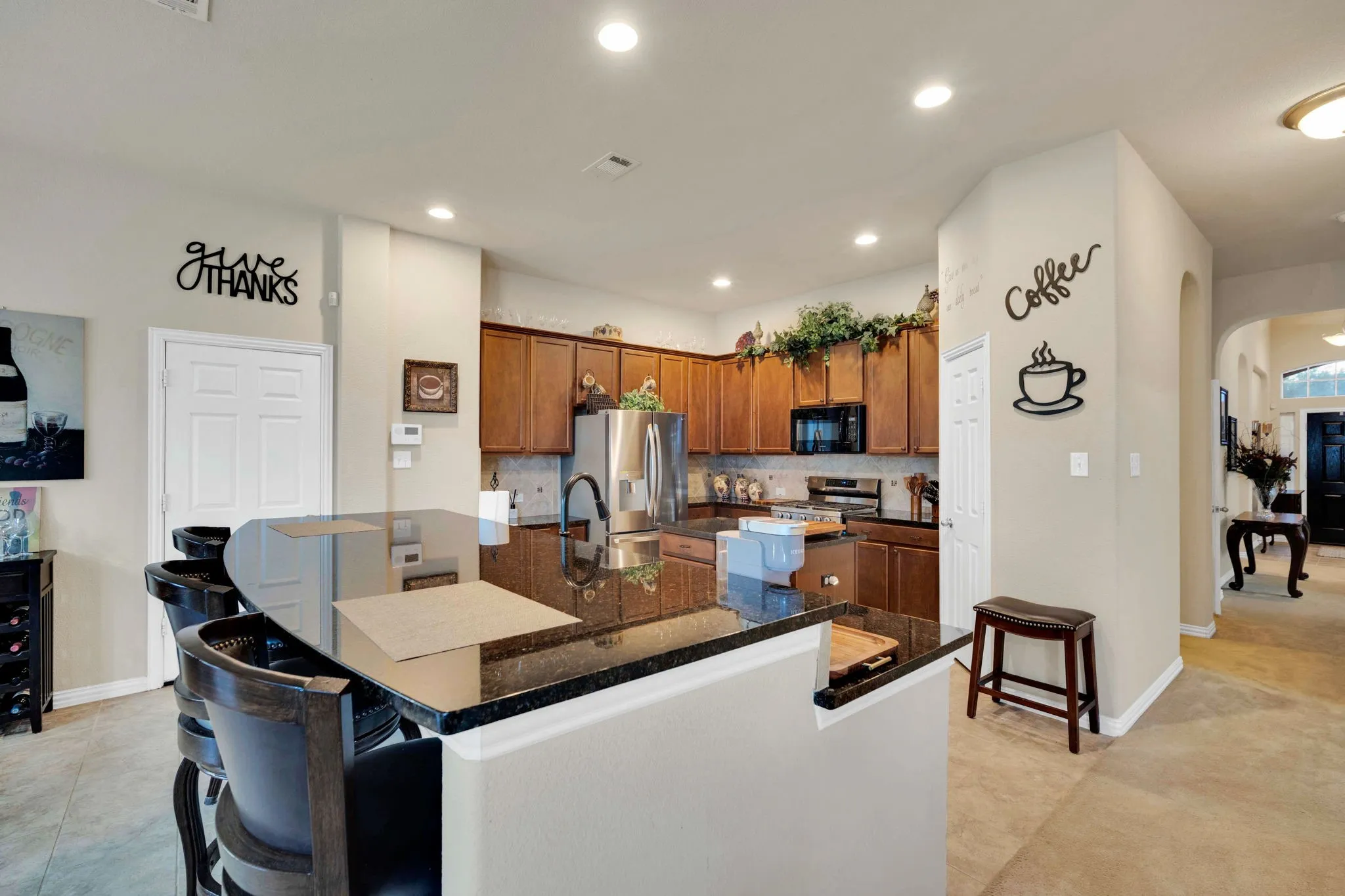 Kitchen featuring a large black countertop island with seating, wood cabinetry, stainless steel appliances, and recessed lighting