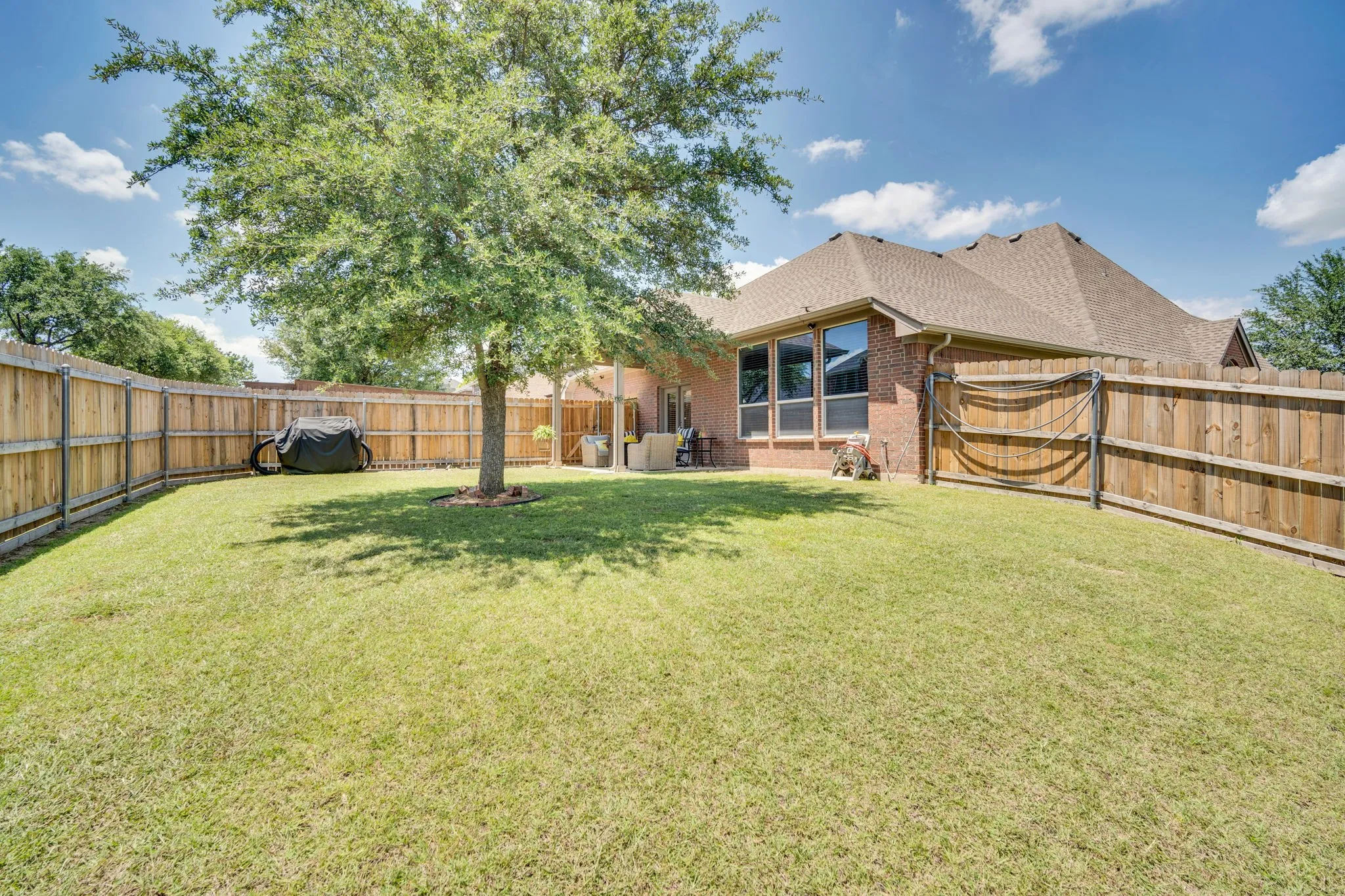 Expansive backyard featuring a mature tree, natural wood privacy fencing, and a brick exterior with multiple windows