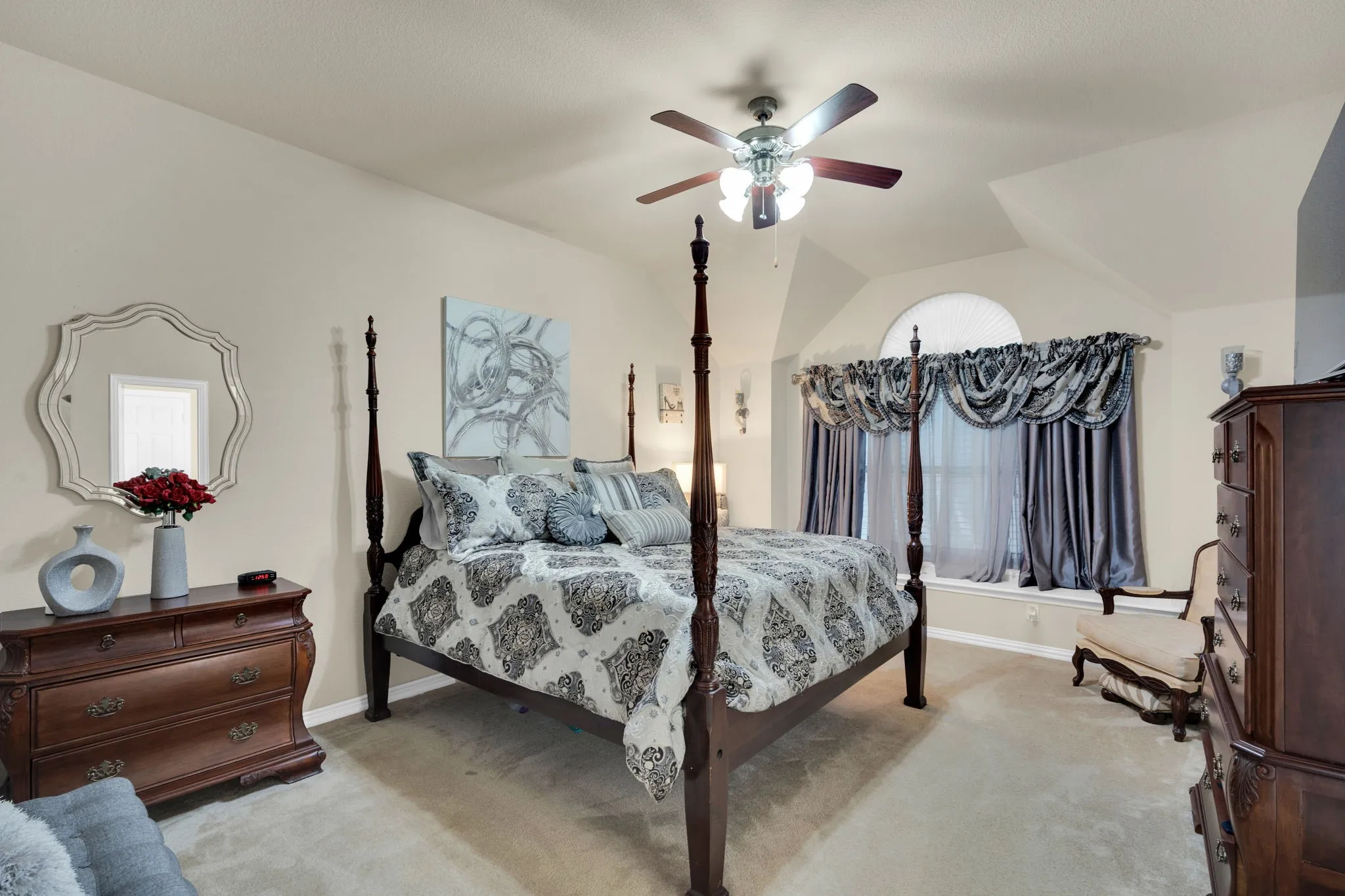 Bedroom featuring vaulted ceilings, a ceiling fan, arched window, wall sconces, and neutral-toned carpeting