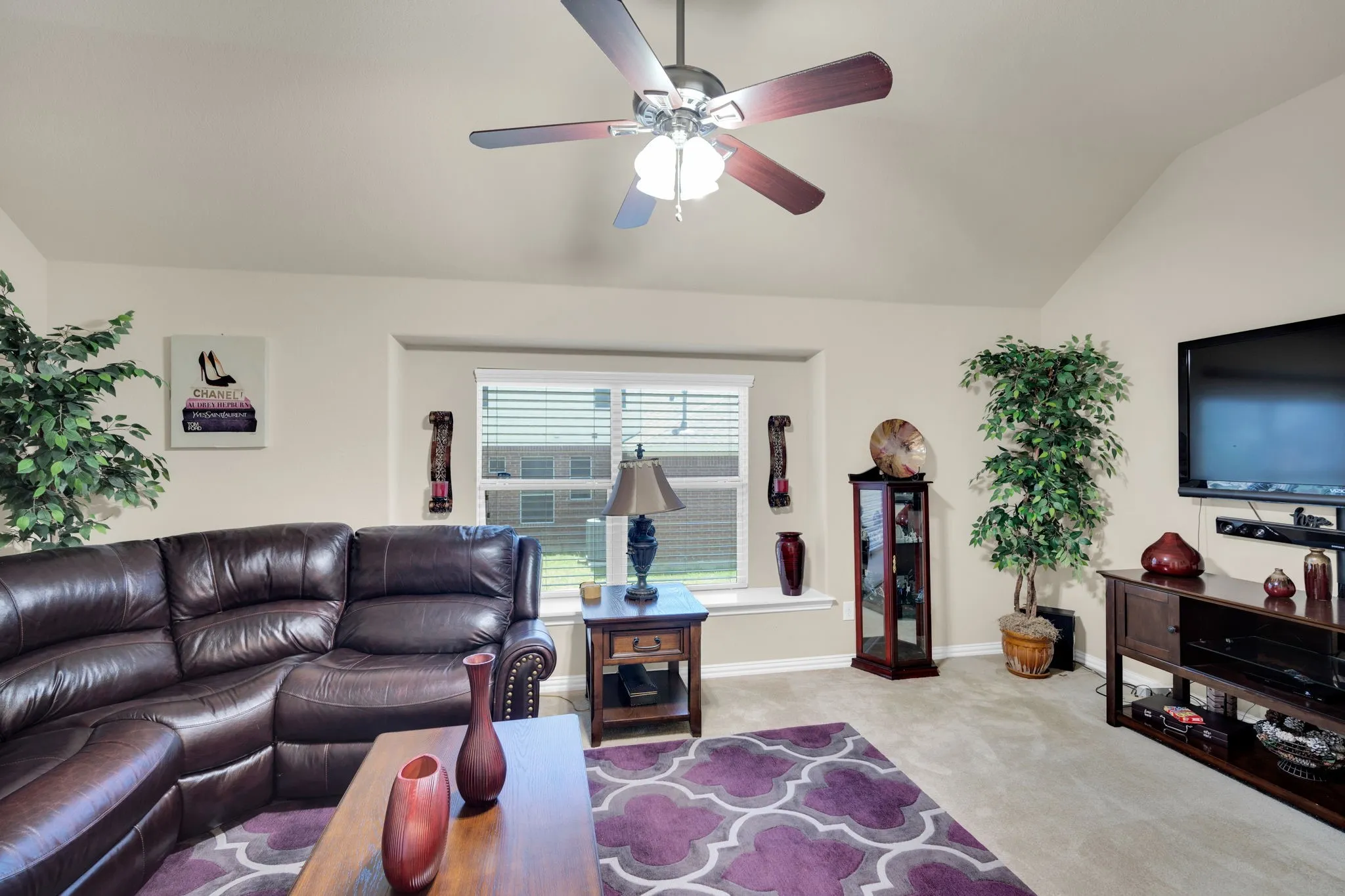 Spacious living area featuring neutral carpeting, a vaulted ceiling, and a ceiling fan with light fixture