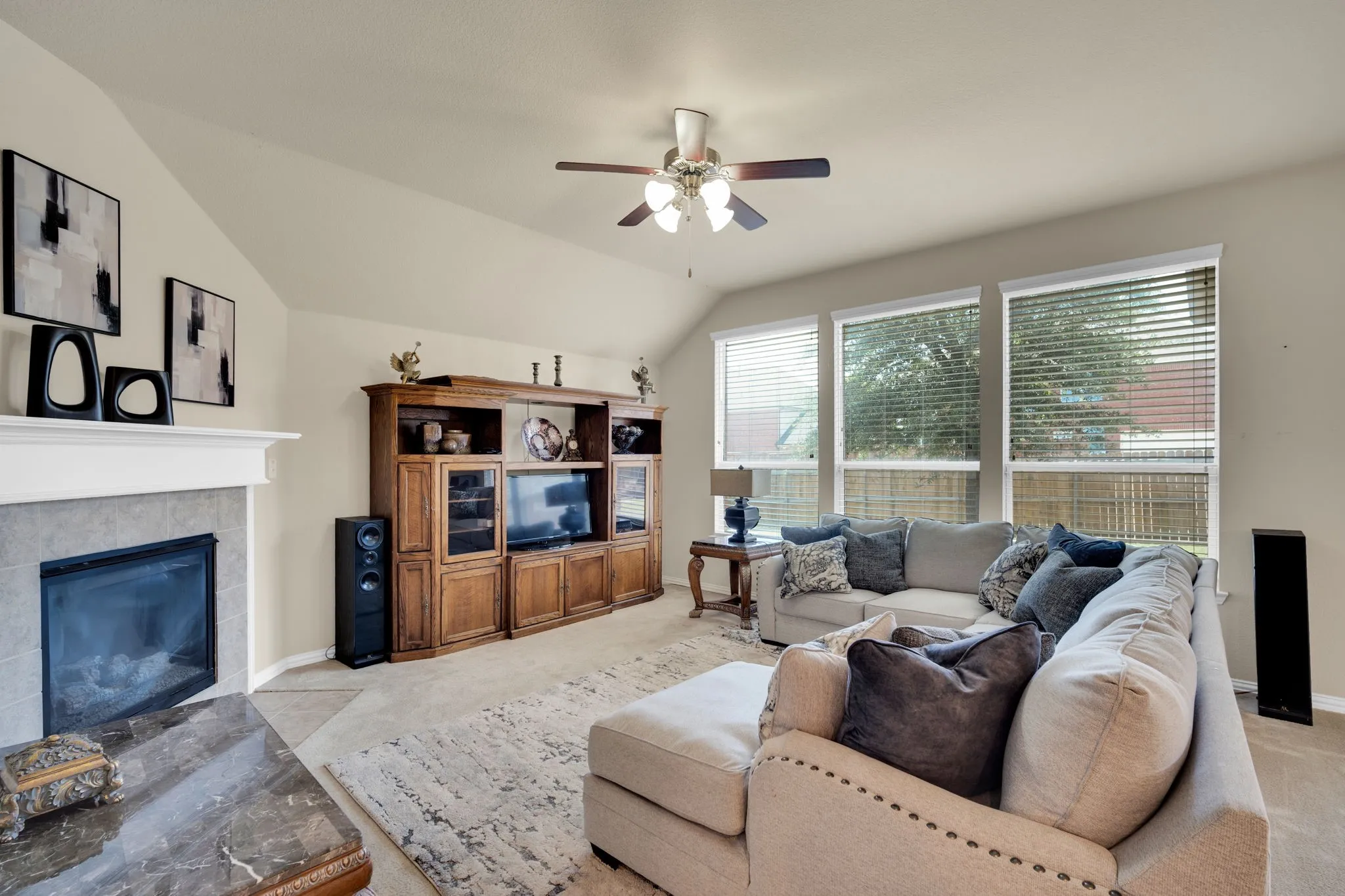Living area featuring a fireplace with a white mantel and tile surround, vaulted ceilings, and three large windows