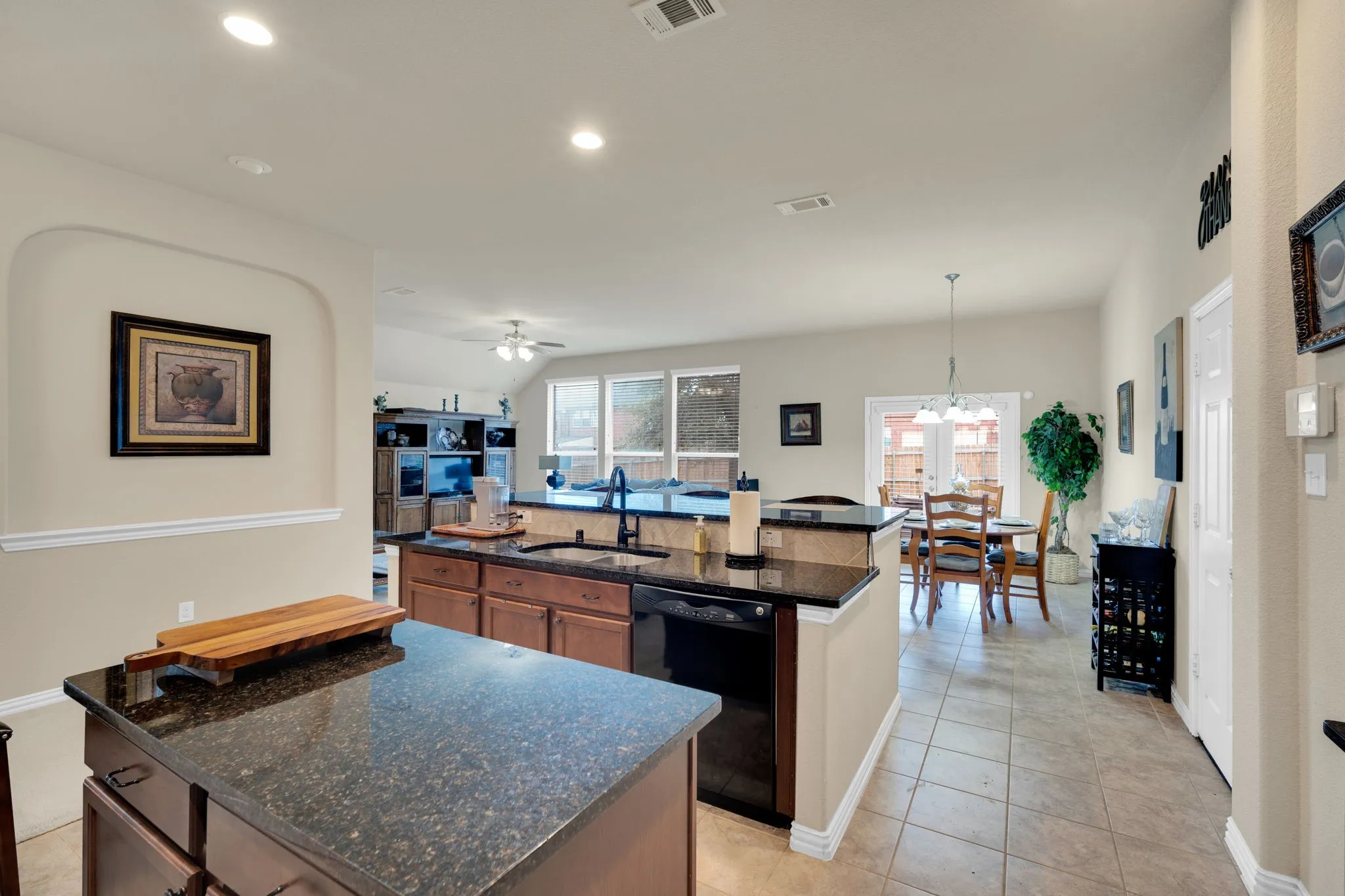 Kitchen featuring an island, black granite countertops, wood cabinetry, built-in dishwasher, and a double basin sink with a high-arch faucet