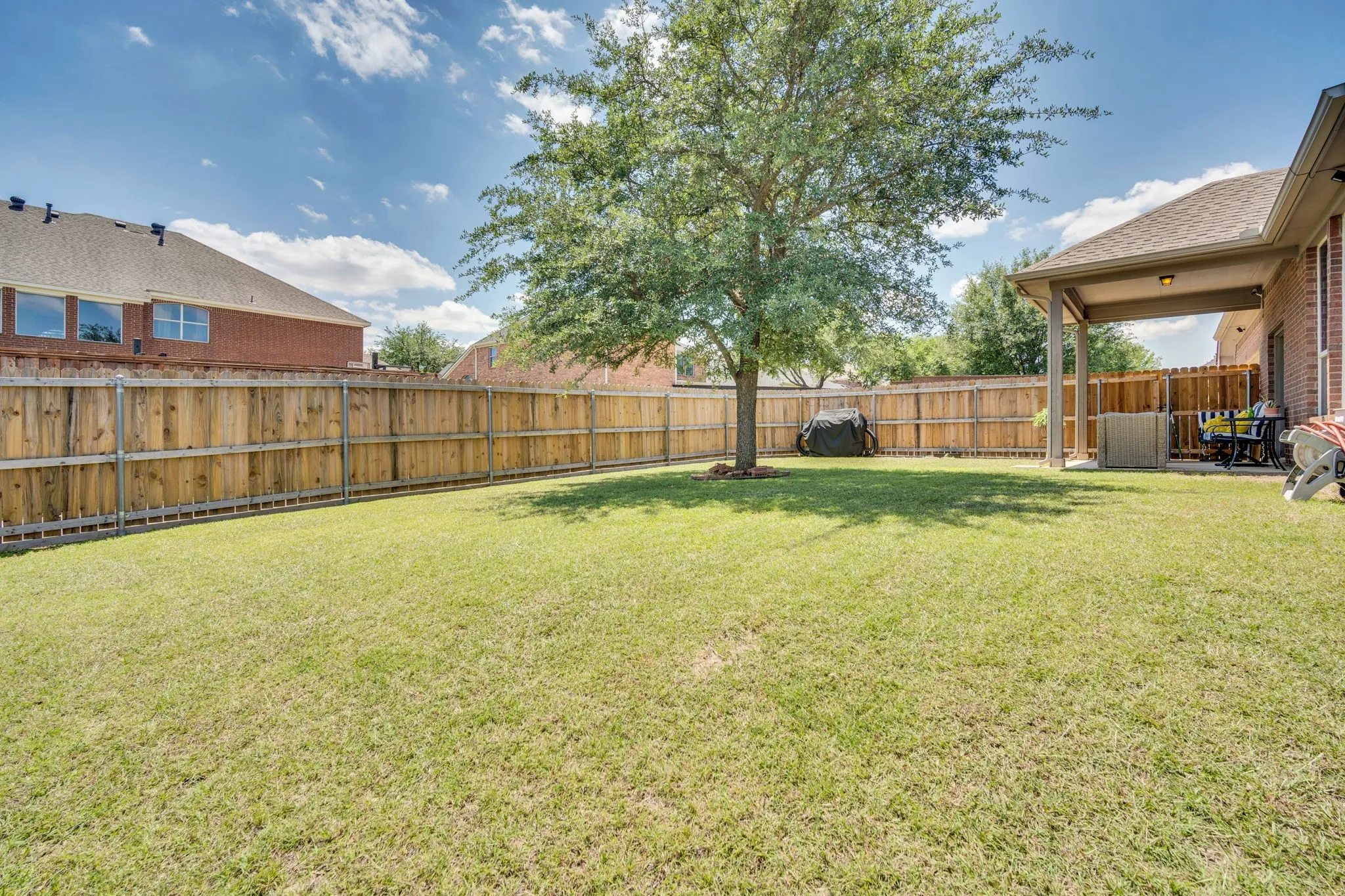 Expansive backyard featuring a manicured lawn, established tree, and a covered patio area