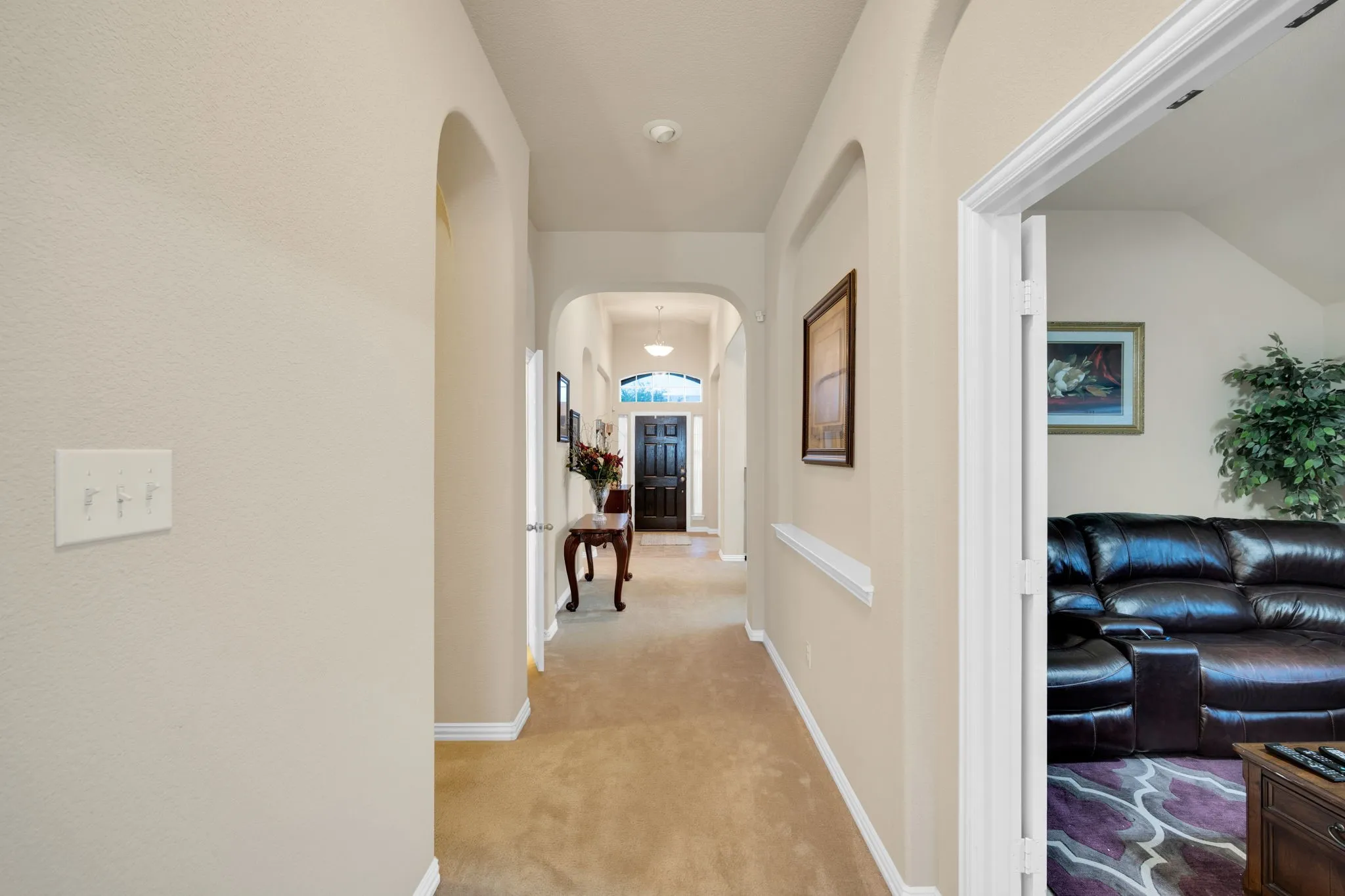 Archway-defined hallway featuring light-toned walls, carpet flooring, crown molding, and white trim