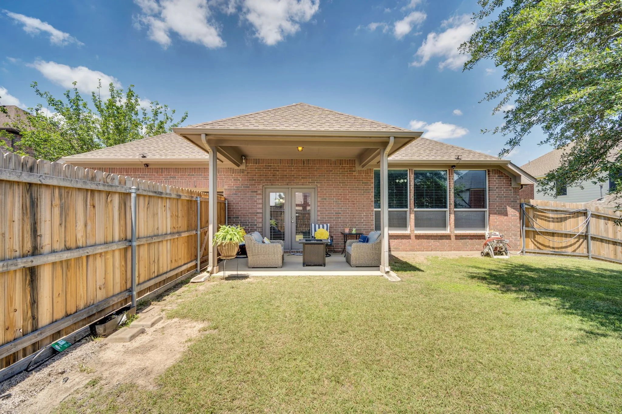 Expansive backyard featuring a covered patio, brick exterior, large windows, and a wood privacy fence